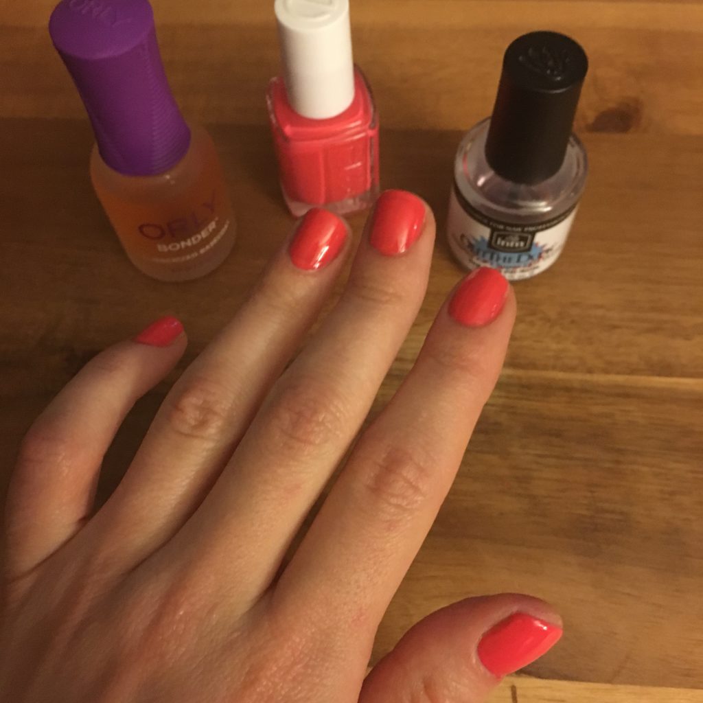 Glass of Glam Nails | At Home Manicure Tips by popular Chicago beauty blog, Glass of Glam: image of a woman's hand next to a bottle of Amazon Orly Base Nail Coat, Amazon essie Nail Polish, Glossy Shine Finish, Peach Daiquiri, and Amazon Out The Door Top Coat.