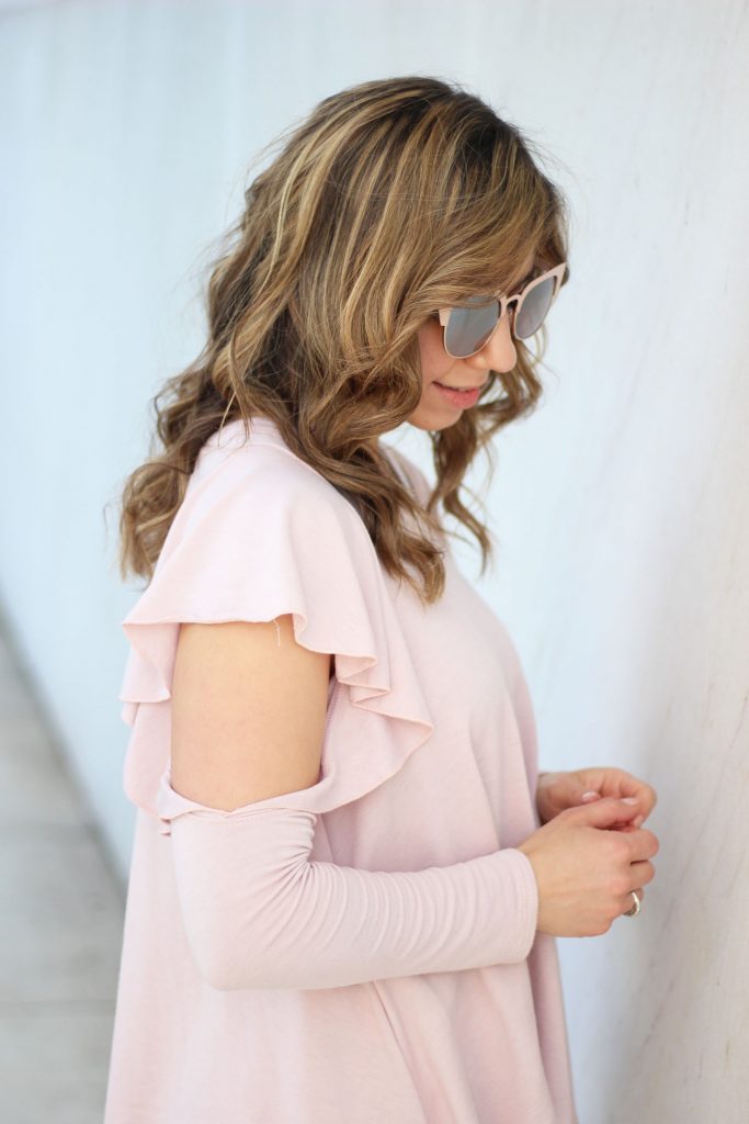 Lifestyle blogger Roxanne Birnbaum of Glass of Glam wearing a Red Dress Boutique pink ruffle top, Old Naby distressed denim, and a JustFab rose gold bag