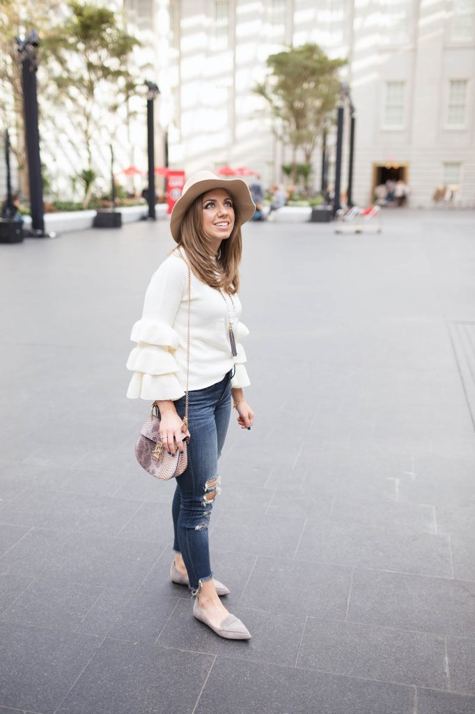 Lifestyle Blogger Roxanne Birnbaum of Glass of Glam wearing a Shein ruffle sweater, saddle bag, M.Gemi flats, and Express distressed denim