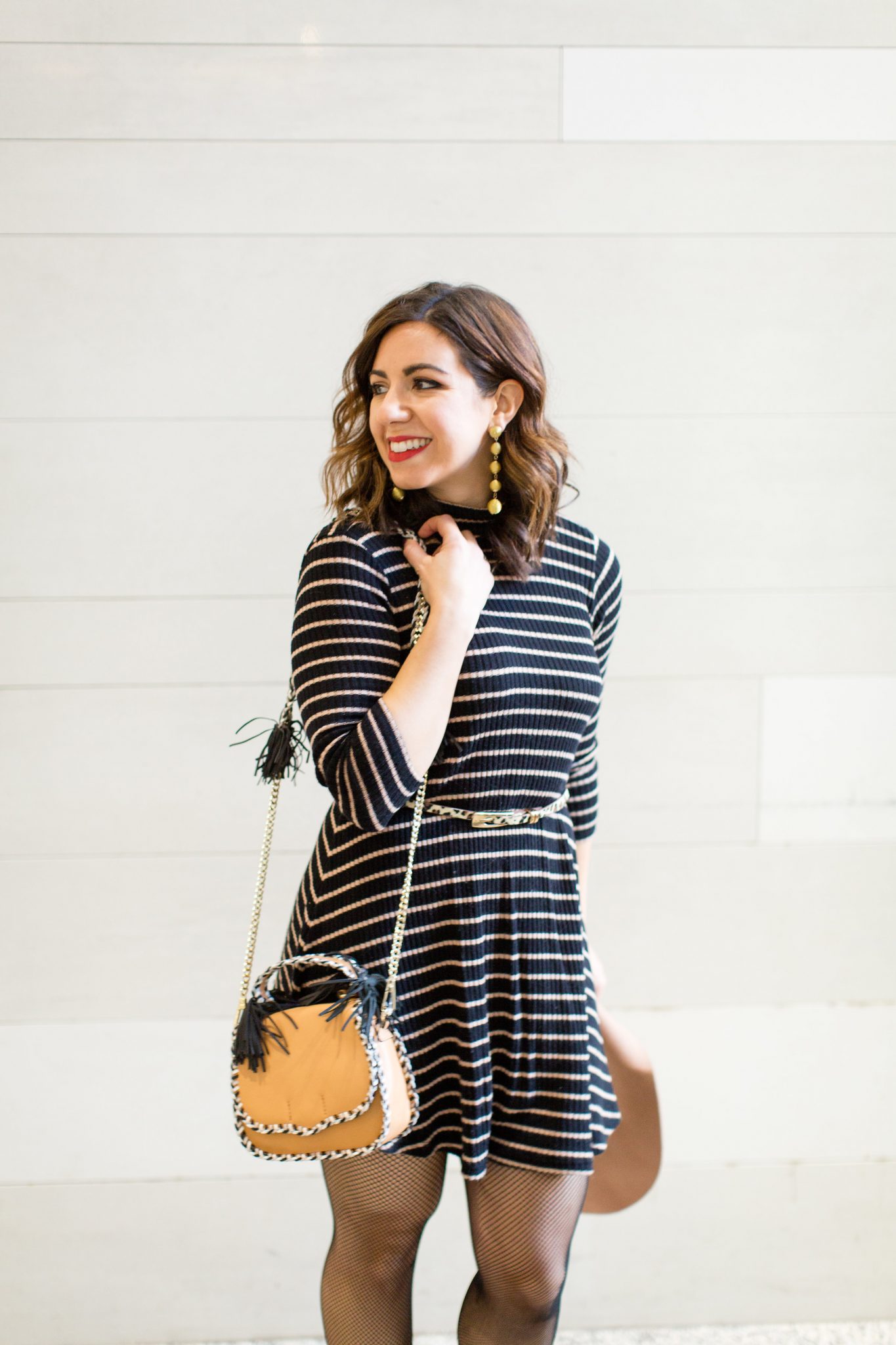 Lifestyle blogger Roxanne of Glass of Glam wearing a striped dress, Rebecca Minkoff bag, ted slouch booties, and fishnet tights