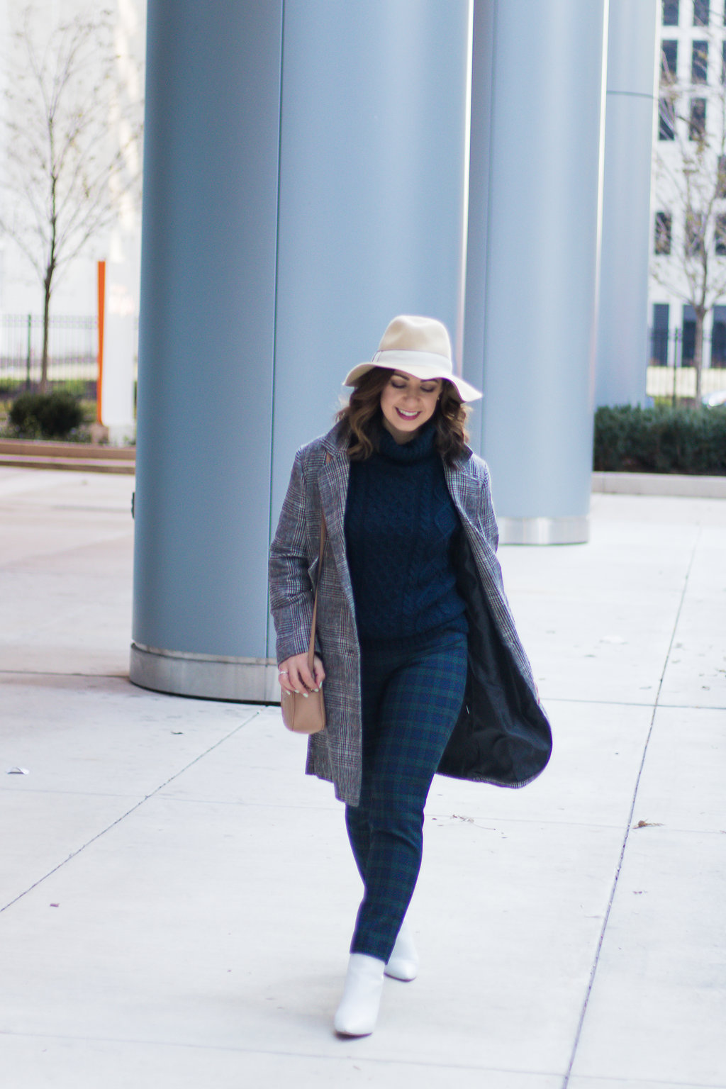 Lifestyle blogger Roxanne of Glass of Glam wearing plaid pants, a plaid coat, felt fedora, white booties, and a cable knit sweater