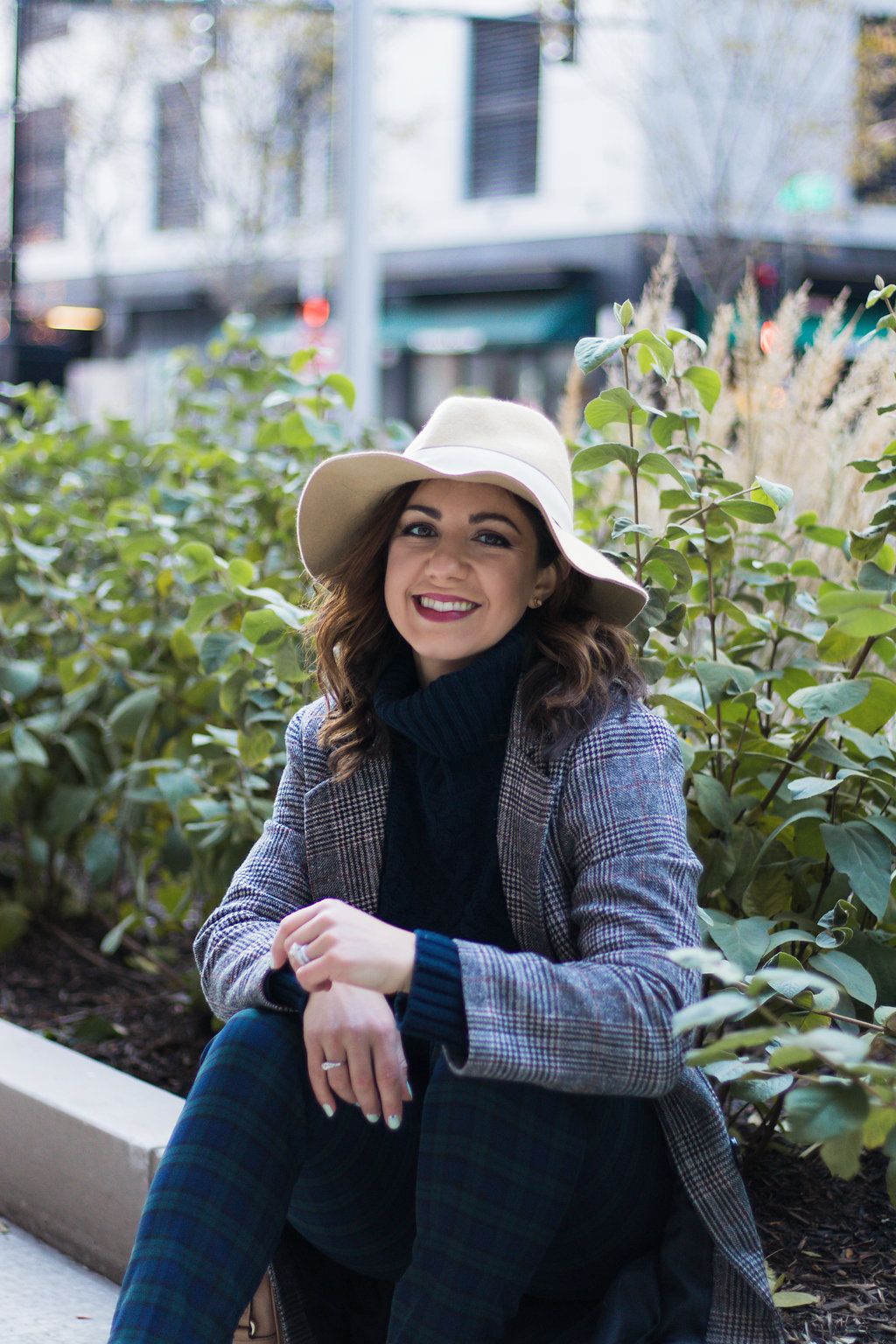 Lifestyle blogger Roxanne of Glass of Glam wearing plaid pants, a plaid coat, felt fedora, white booties, and a cable knit sweater