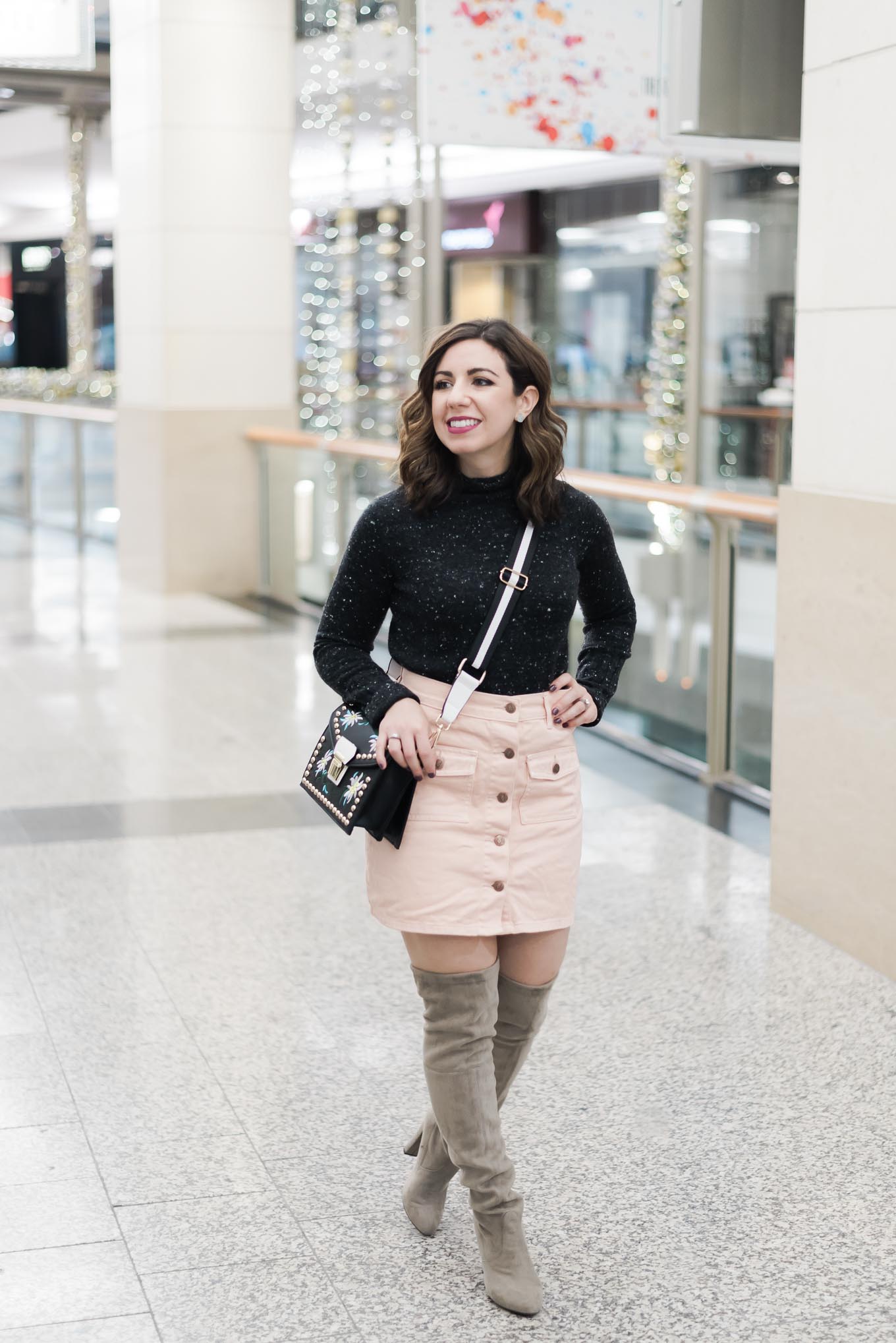 Lifestyle blogger Roxanne of Glass of Glam wearing a MINKPINK denim skirt, otk boots, a Madewell sweater, pom hat, and a rivet crossbody bag