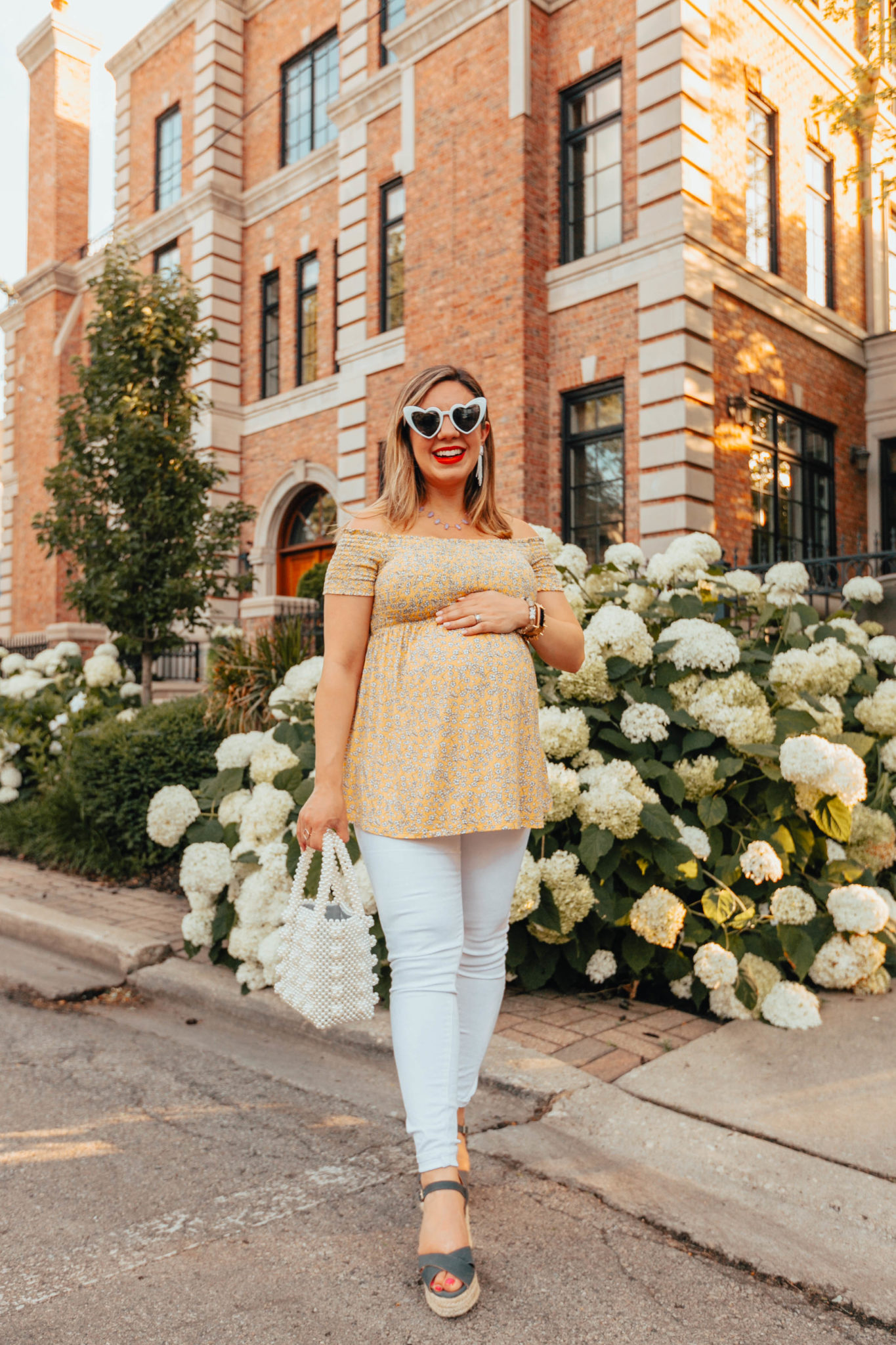 Summer maternity outfit featured by top US fashion log, Glass of Glam: image of a pregnant woman wearing an Ingrid & Isabel off the shoulder flower top, Old Nave Maternity white denim, Castaner low wedges, Miuco pearl tote bag, Kendra Scott necklace, SUGARFIX beaded earrings, and MINCL heart sunglasses.