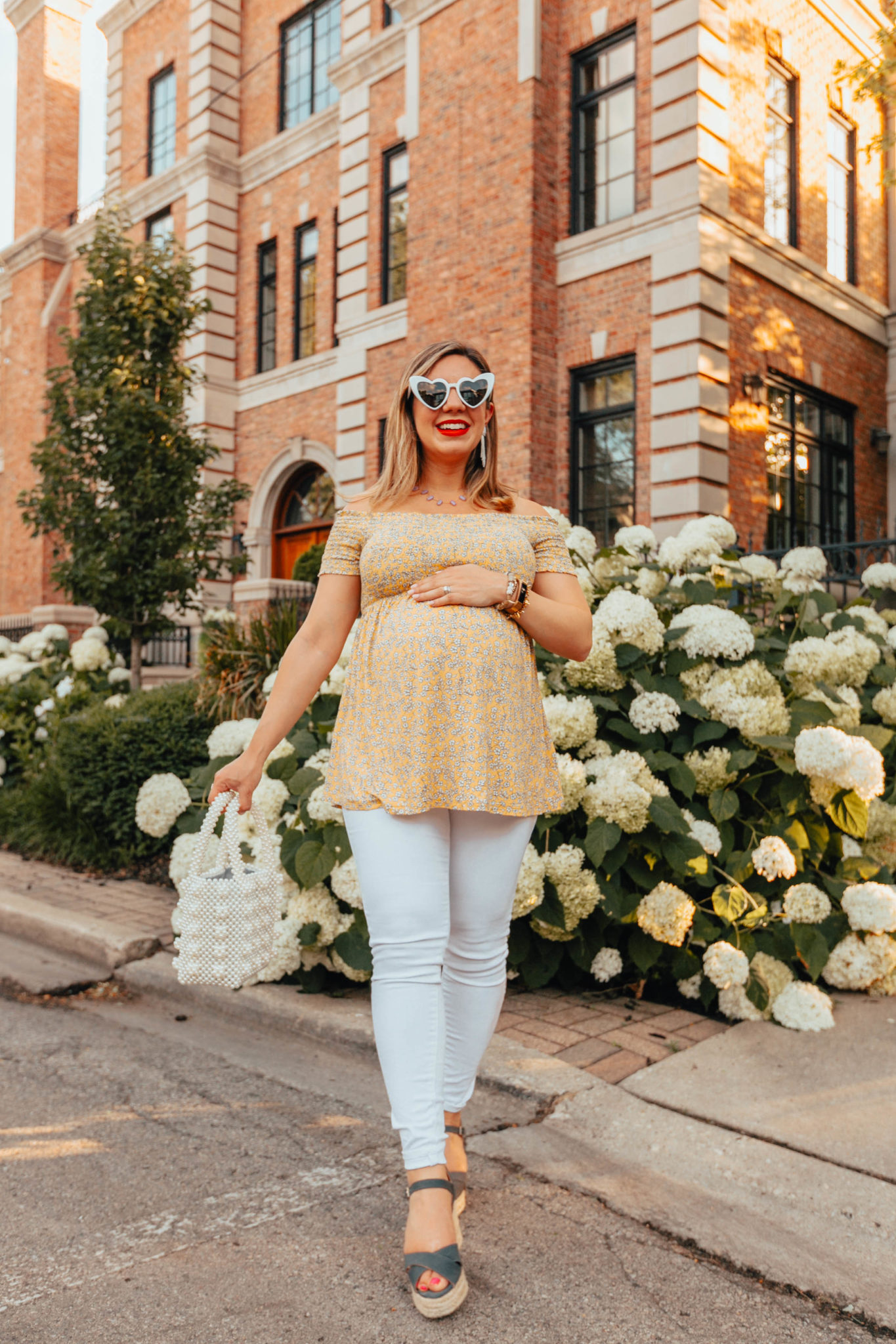 Summer maternity outfit featured by top US fashion log, Glass of Glam: image of a pregnant woman wearing an Ingrid & Isabel off the shoulder flower top, Old Nave Maternity white denim, Castaner low wedges, Miuco pearl tote bag, Kendra Scott necklace, SUGARFIX beaded earrings, and MINCL heart sunglasses.