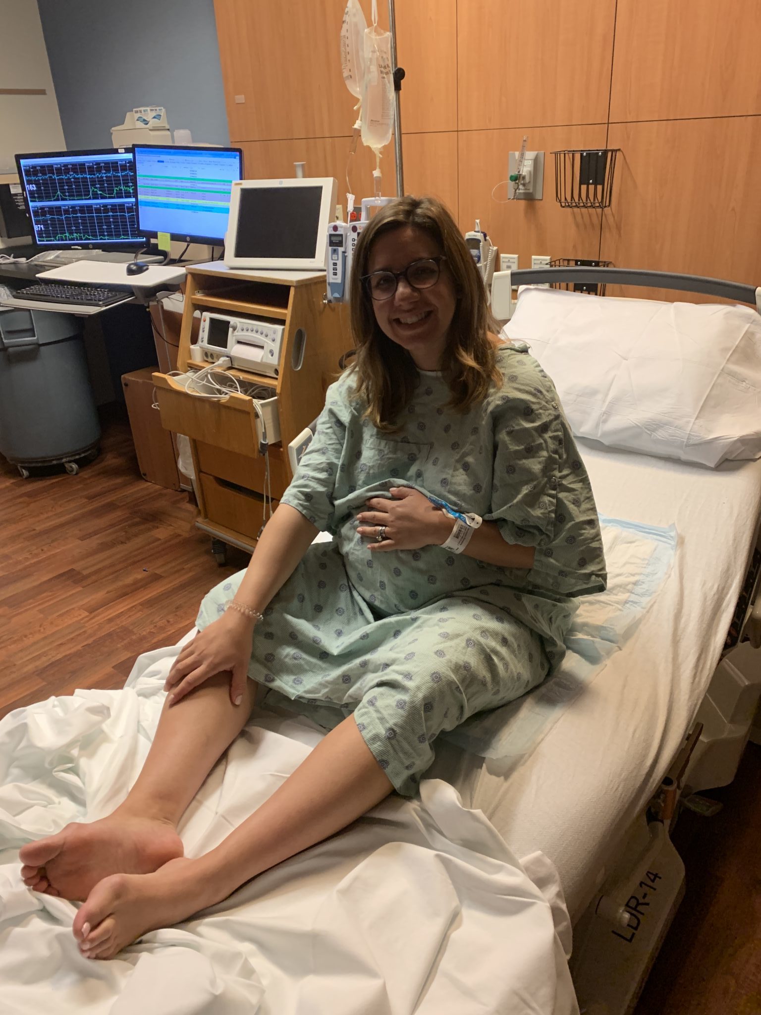 Baby Girl Birth Story: Welcome Sidney Eileen! by popular life and style blog, Glass of Glam: image of a woman wearing a hospital gown and sitting in a bed in a labor and delivery room at the hospital.