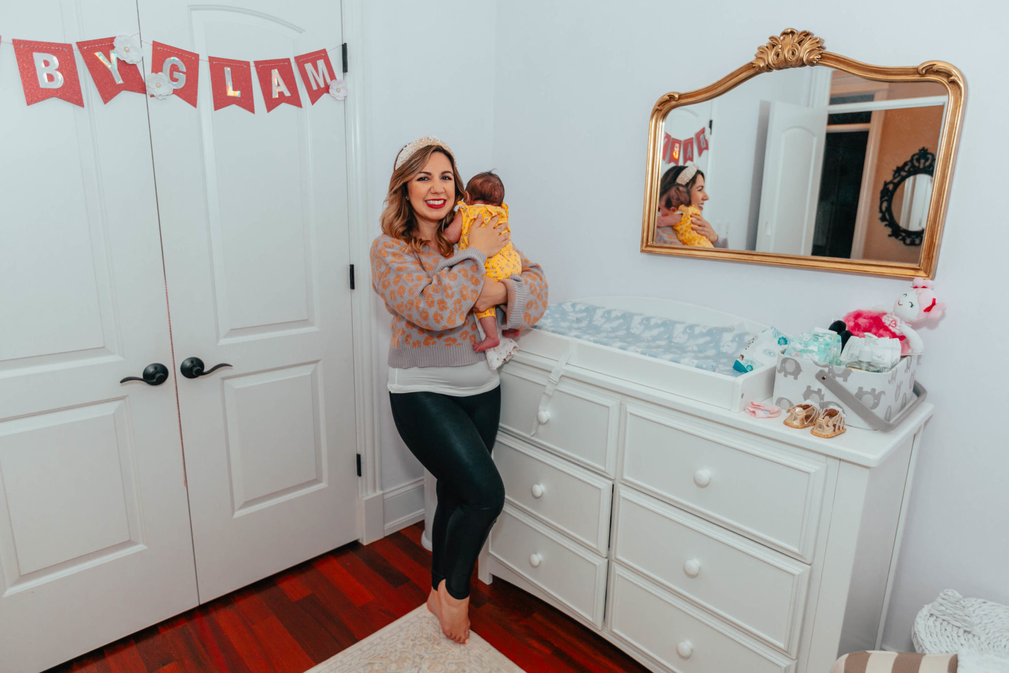 My Favorite Newborn Essentials by popular life and style blog, Glass of Glam: image of a woman holding her baby next to a changing table in the baby nursery. 