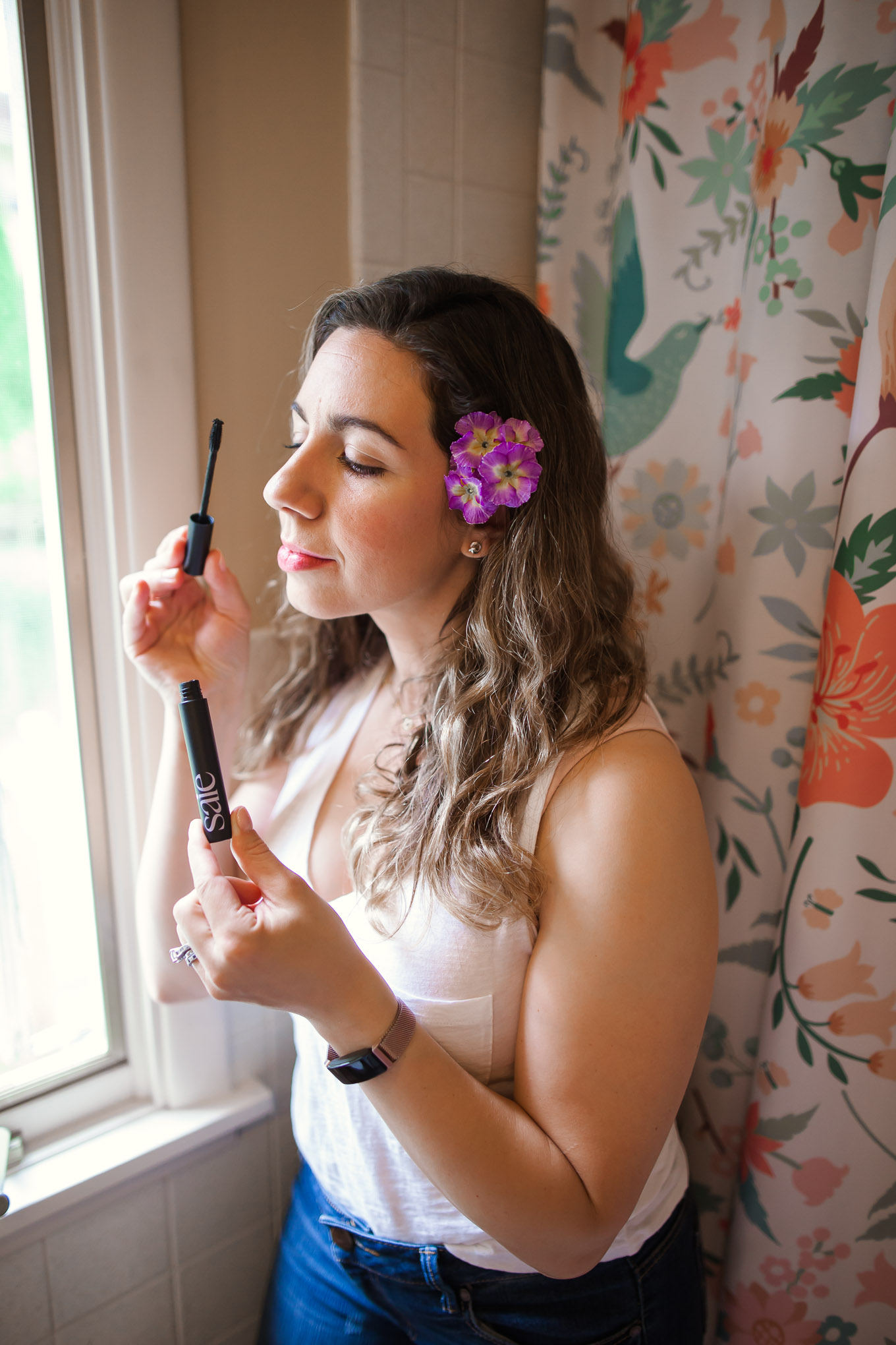 Clean Beauty by popular Chicago beauty blog, Glass of Glam: image of a woman in a white tank top and jeans and standing in front of a floral shower curtain while wearing RMS Beauty Un Cover-Up, Saie Mascara, Ere Perez Lip and Cheek Tint, RMS Beauty Lip2Cheek, Ilia Brow Gel, RMS Beauty Magic Luminizer