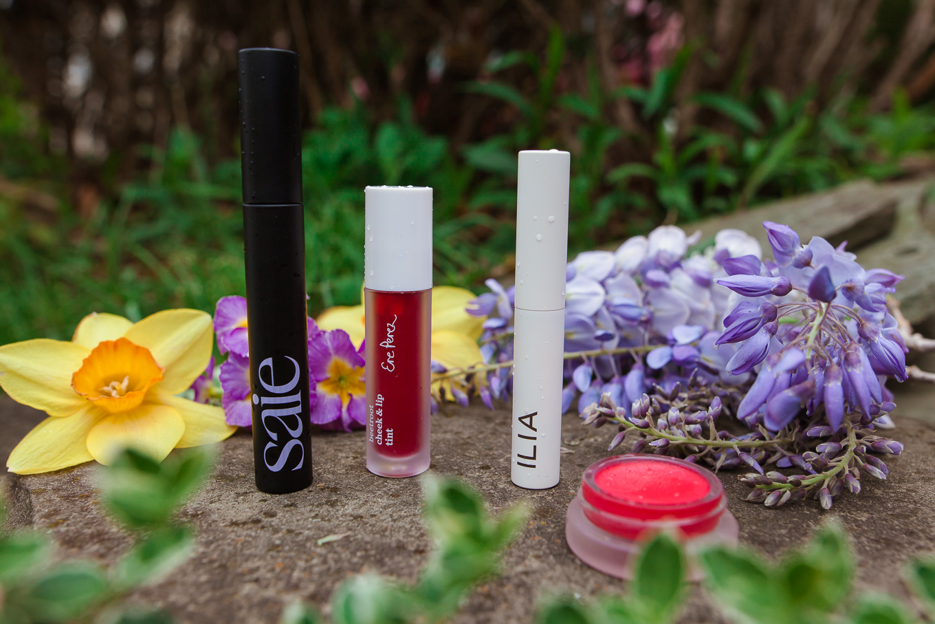 Clean Beauty by popular Chicago beauty blog, Glass of Glam: image of Saie Mascara, Ere Perez Lip and Cheek Tint, and Ilia Brow Gel next to some daffodil and lilac blossoms. 