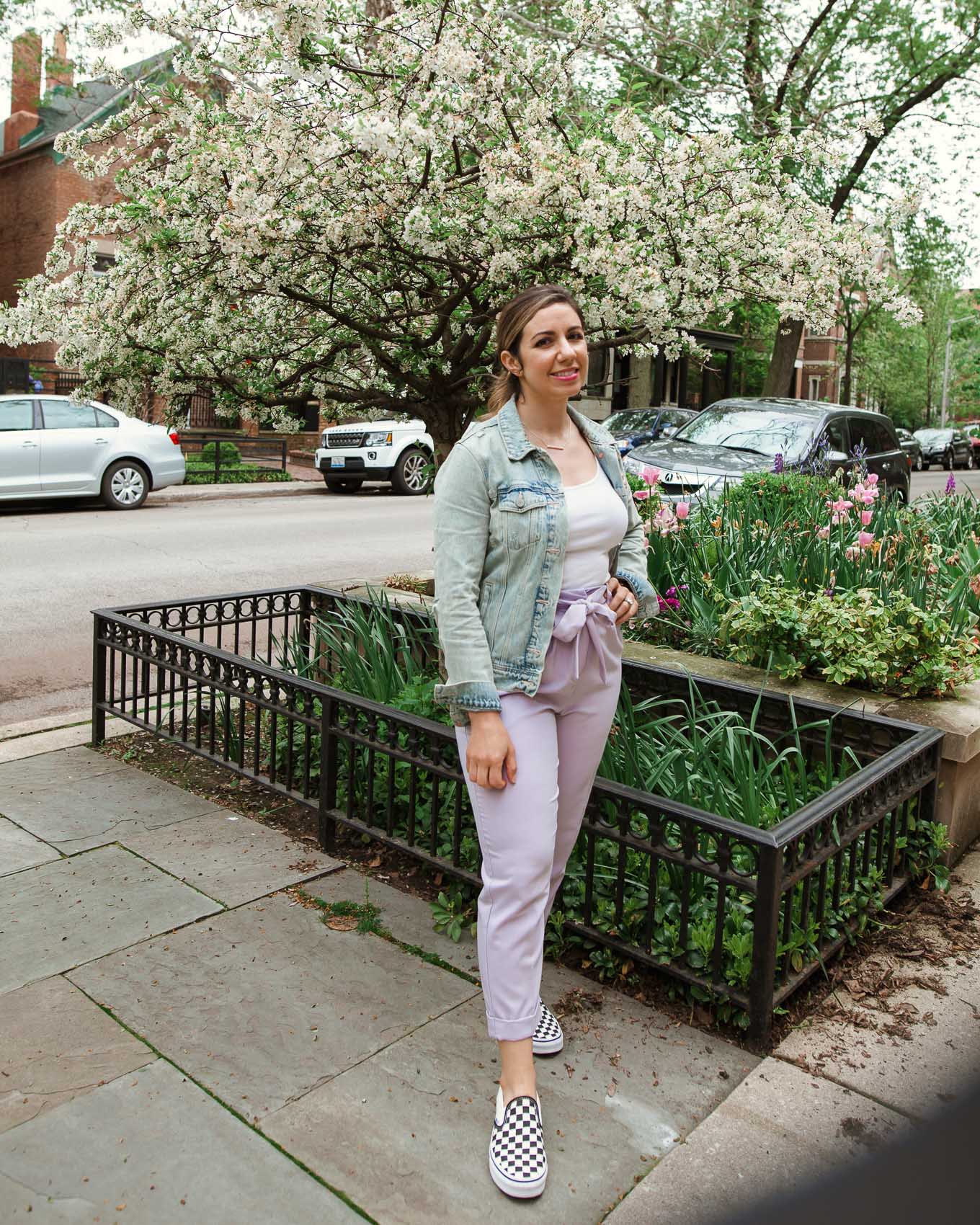 Tie Waist Pants by popular Chicago fashion blog, Glass of Glam: image of a woman standing outside by some white tulips and wearing a pair of lavender tie waist pants, Old Navy First-Layer Slim-Fit Rib-Knit Tank Top for Women, Old Navy Distressed Jean Jacket for Women, Nordstrom Classic Slip-On Sneaker VANS, and Kendra Scott Kelsey Pendant Necklace In Rose Gold.