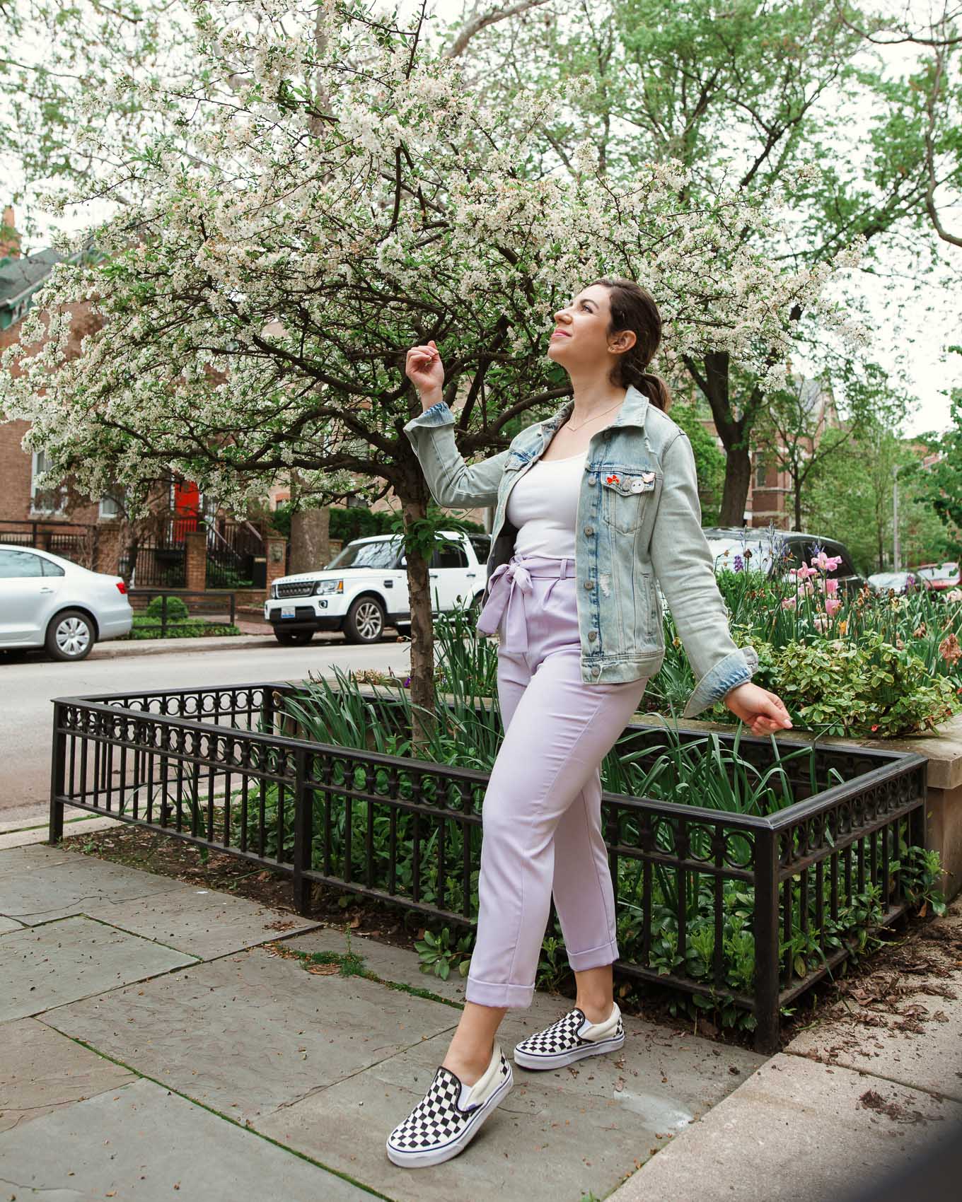 Tie Waist Pants by popular Chicago fashion blog, Glass of Glam: image of a woman standing outside by some white tulips and wearing a pair of lavender tie waist pants, Old Navy First-Layer Slim-Fit Rib-Knit Tank Top for Women, Old Navy Distressed Jean Jacket for Women, Nordstrom Classic Slip-On Sneaker VANS, and Kendra Scott Kelsey Pendant Necklace In Rose Gold.