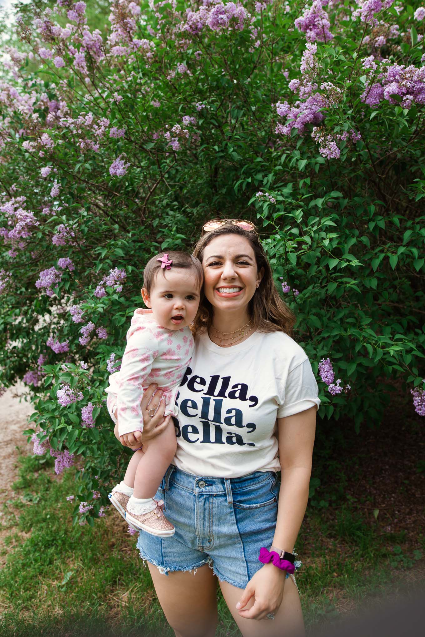 Link Up by popular Chicago lifestyle blog, Glass of Glam: image of a woman holding her baby while standing next to a lilac bush and wearing a Bella t-shirt, Abercrombie & Fitch High Rise Mom Shorts, Monica + Andy Long Sleeve Jack + Jill Bodysuit, and Keds Little Kid's Keds x kate spade new york Champion Glitter Crib Sneaker.