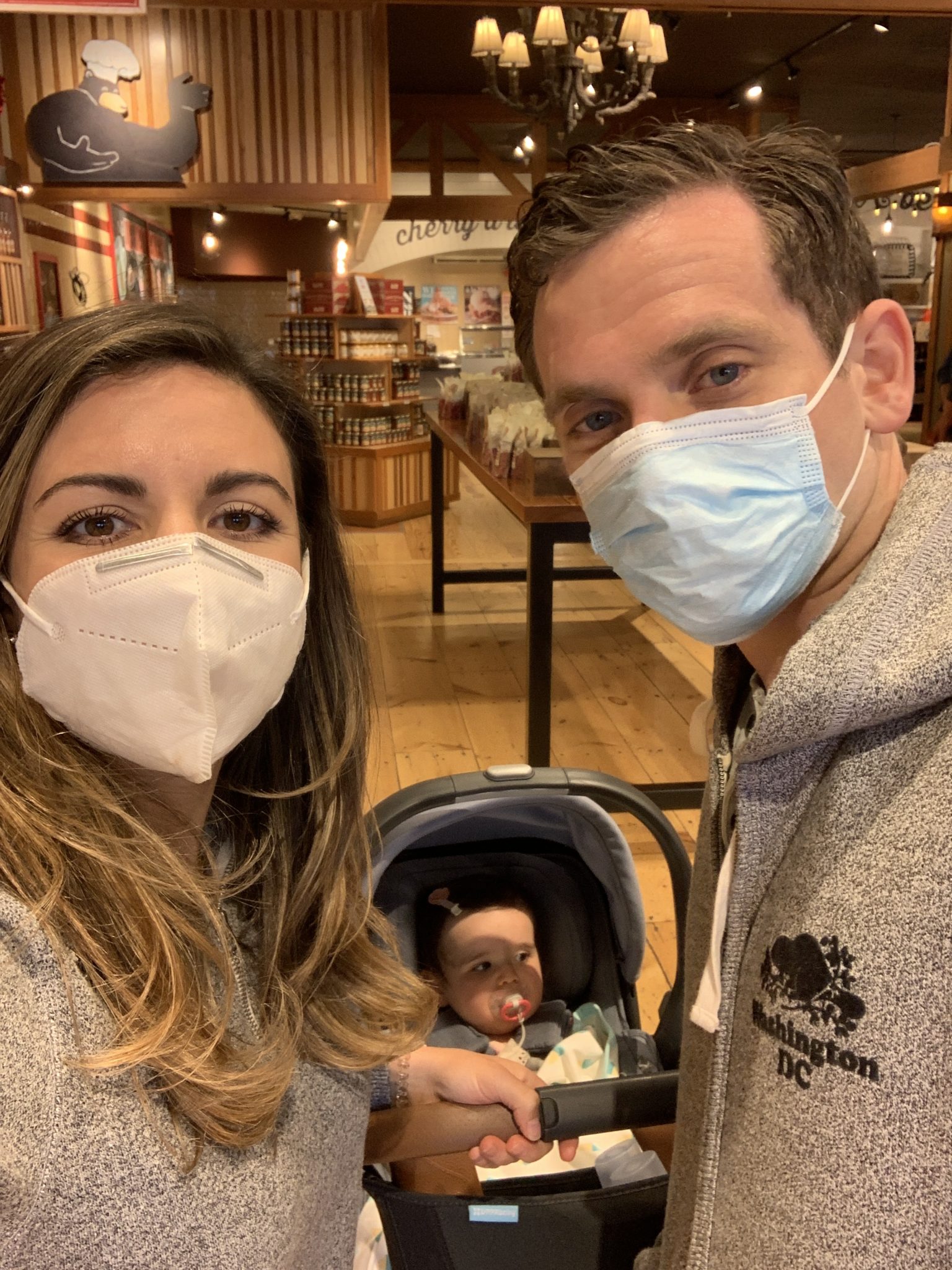 Traverse City by popular Chicago travel blog, Glass of Glam: image of a mom and dad wearing masks and holding their baby daughter in her car seat.