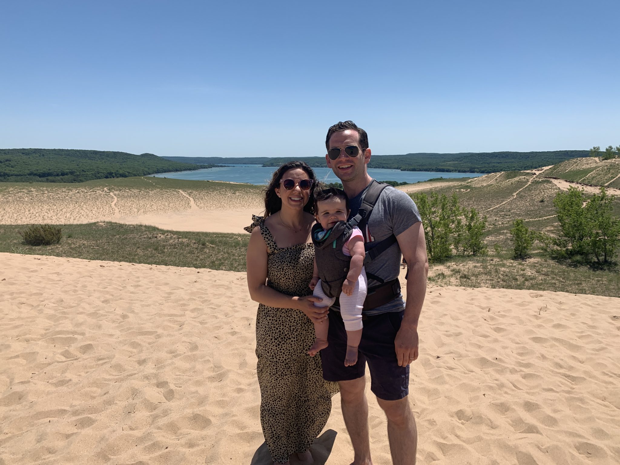 Traverse City by popular Chicago travel blog, Glass of Glam: image of a husband, wife and their baby daughter standing on a sand dune. 