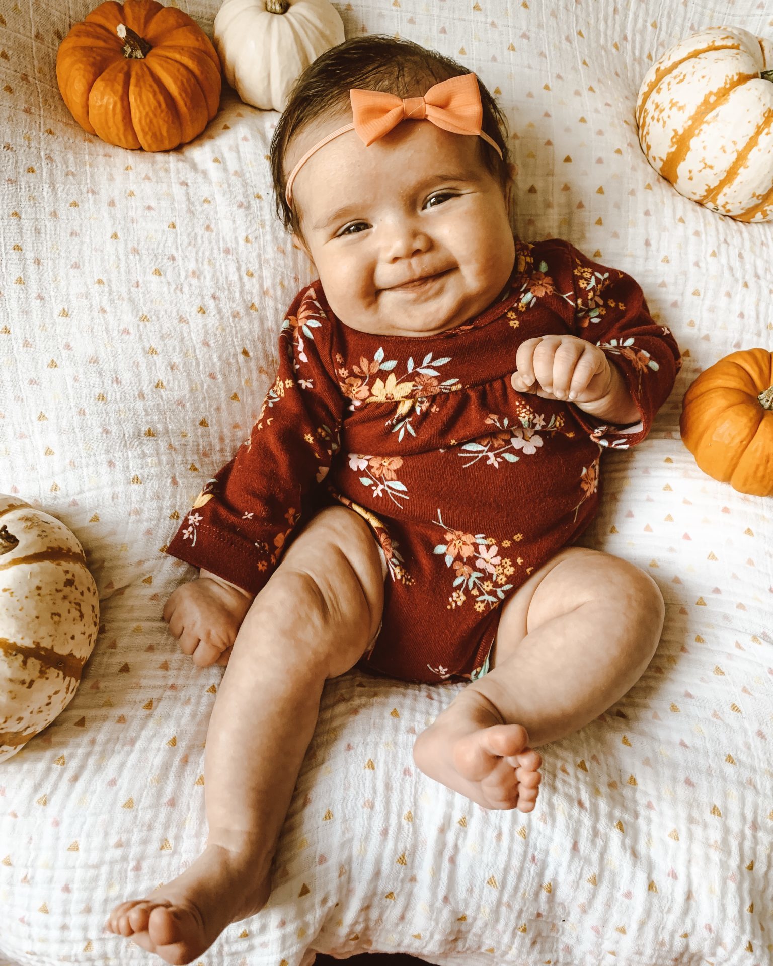 First Birthday by popular Chicago motherhood blog, Glass of Glam: image of a two month old baby girl lying on a muslin blanket and surround by mini pumpkins.