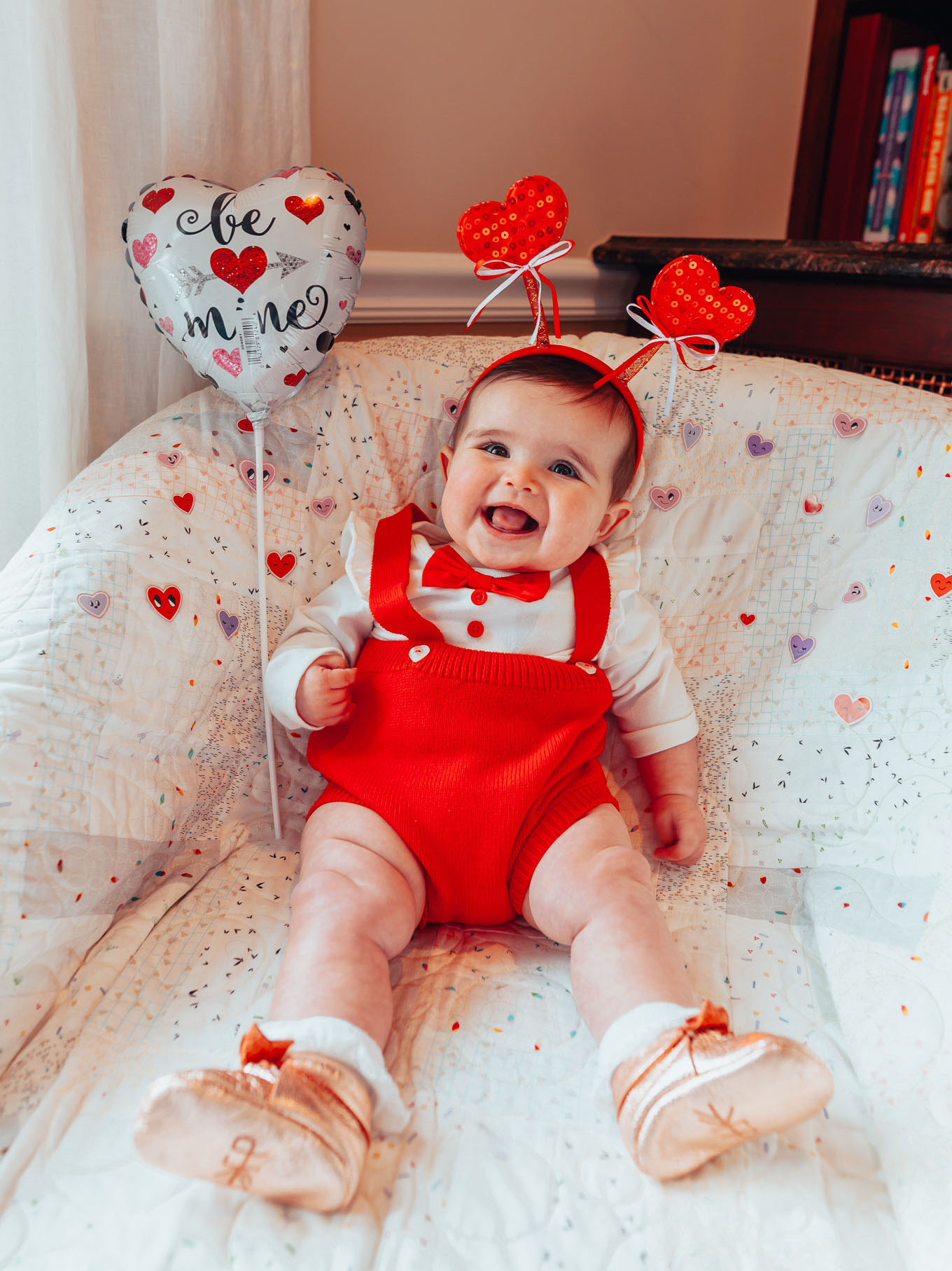 First Birthday by popular Chicago motherhood blog, Glass of Glam: image of a 6 month old baby girl wearing a heart head band, red romper and sitting next to a heart shaped balloon.