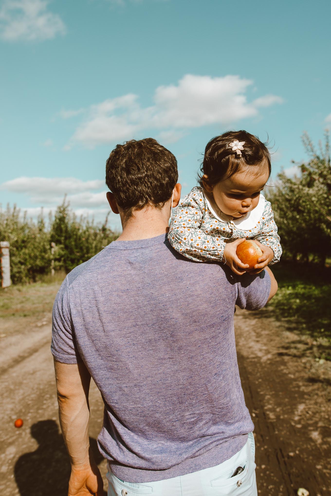 Apple Picking by popular Chicago lifestyle blog, Glass of Glam: image of a dad holding his 1 year old daughter at Apple Holler while she eats an apple.