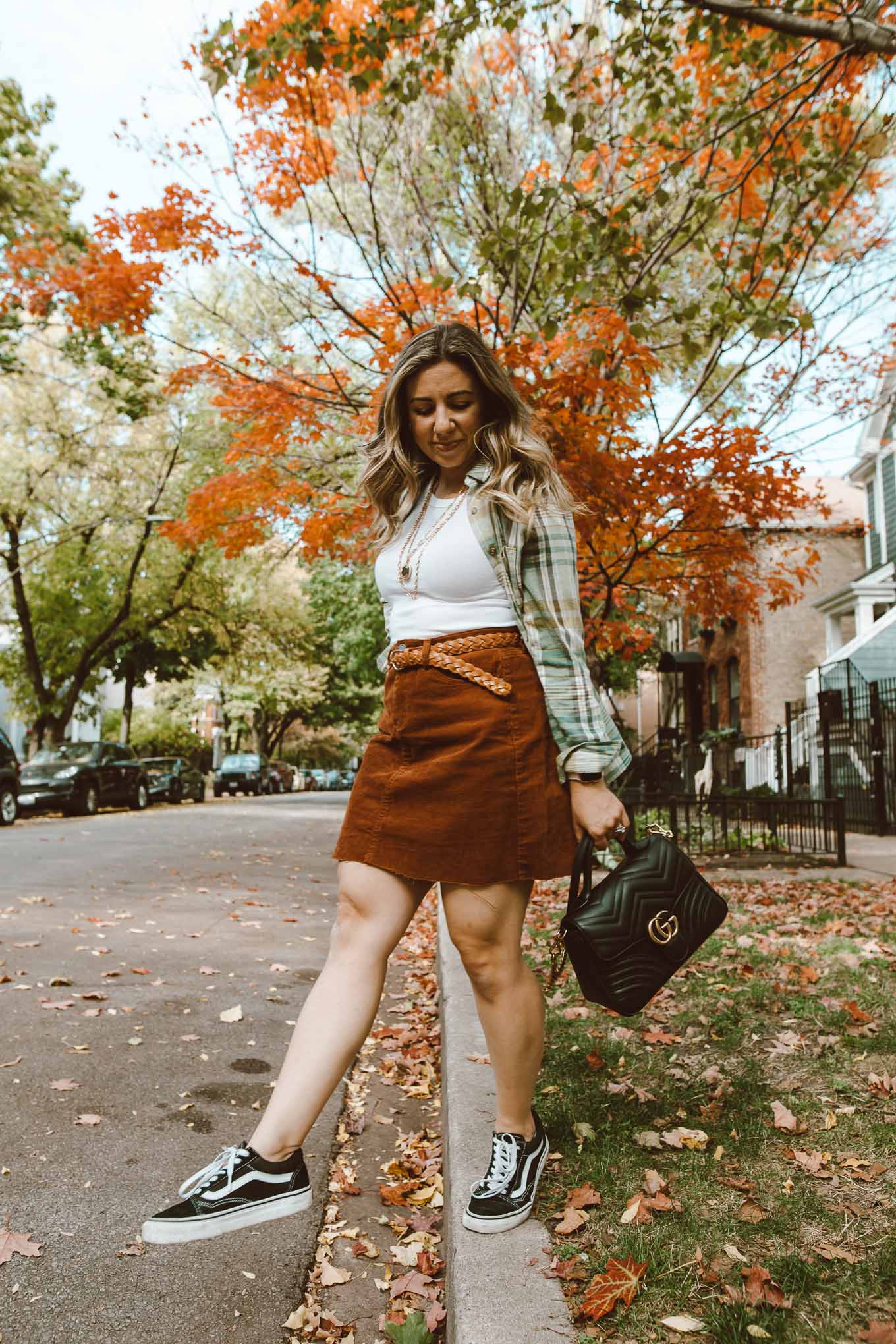 90's Fashion by popular Chicago fashion blog, Glass of Glam: image of a woman walking outside and wearing a corduroy skirt, Vans sneakers, flannel shirt, Target white tank top, Kendra Scott Davis Multistrand Necklace, and holding a Gucci bag. 