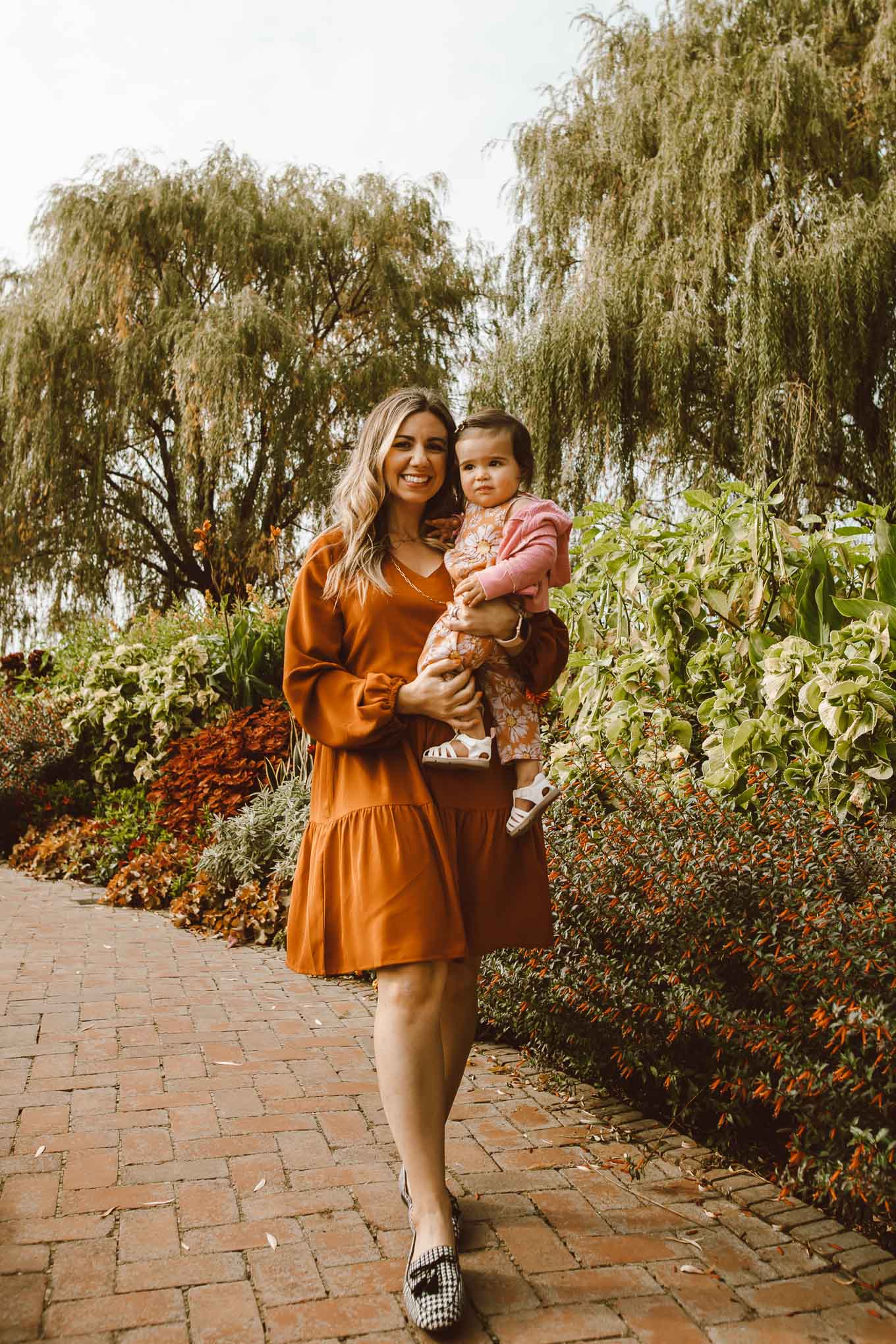 Botanic Garden by popular Chicago fashion blog, Glass of Glam: image of a woman walking through the Chicago Botanic Garden with her daughter and wearing a Amazon Amoretu Women Summer Tunic Dress V Neck Casual Loose Flowy Swing Shift Dresses, Kendra Scott Davis Vintage Gold Multi Strand Necklace In Golden Obsidian and Pat Pat Baby Girl Sunflowers Print Jumpsuits.