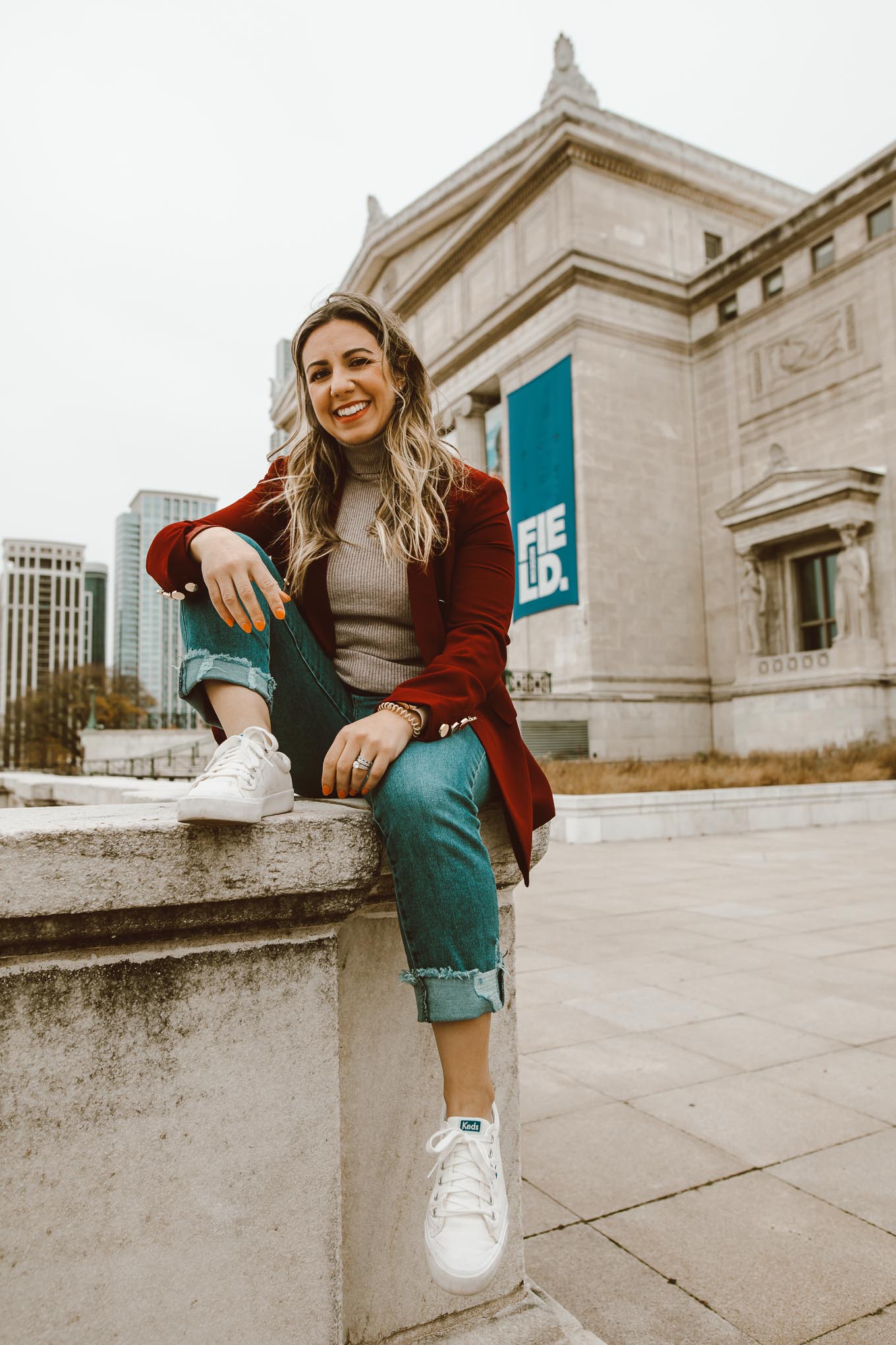 Burgundy Blazer by popular Chicago fashion blog, Glass of Glam: image of a woman sitting outside of the Chicago Field Museum and wearing a burgundy blazer, ribbed turtleneck, jeans, and Keds sneakers. 