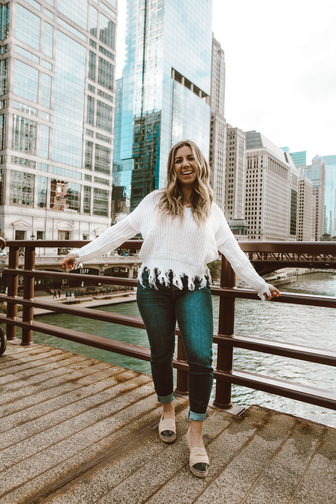 Neutral Colors by popular Chicago fashion blog, Glass of Glam: image of a woman standing outside in downtown Chicago and wearing a Neutral Rebel On the Edge Fringe Sweater, Chanel espadrilles, Neutral Rebel Kancan High-Rise Skinny Jeans in Dark Blue, and Etsy name necklace. 