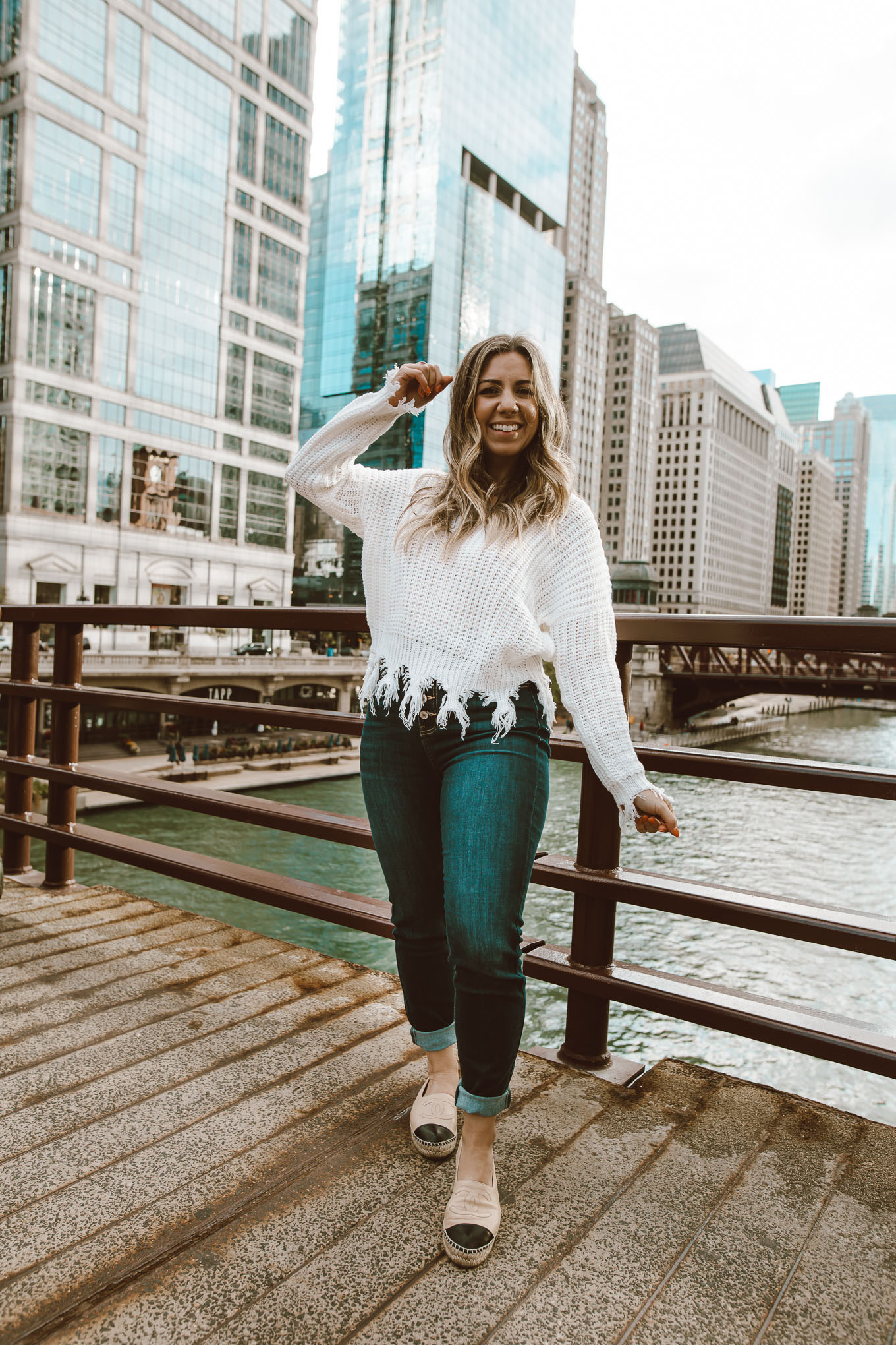 Neutral Colors by popular Chicago fashion blog, Glass of Glam: image of a woman standing outside in downtown Chicago and wearing a Neutral Rebel On the Edge Fringe Sweater, Chanel espadrilles, Neutral Rebel Kancan High-Rise Skinny Jeans in Dark Blue, and Etsy name necklace.
