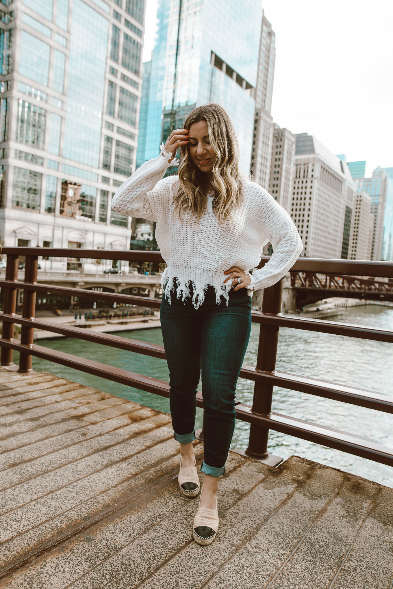 Neutral Colors by popular Chicago fashion blog, Glass of Glam: image of a woman standing outside in downtown Chicago and wearing a Neutral Rebel On the Edge Fringe Sweater, Chanel espadrilles, Neutral Rebel Kancan High-Rise Skinny Jeans in Dark Blue, and Etsy name necklace.