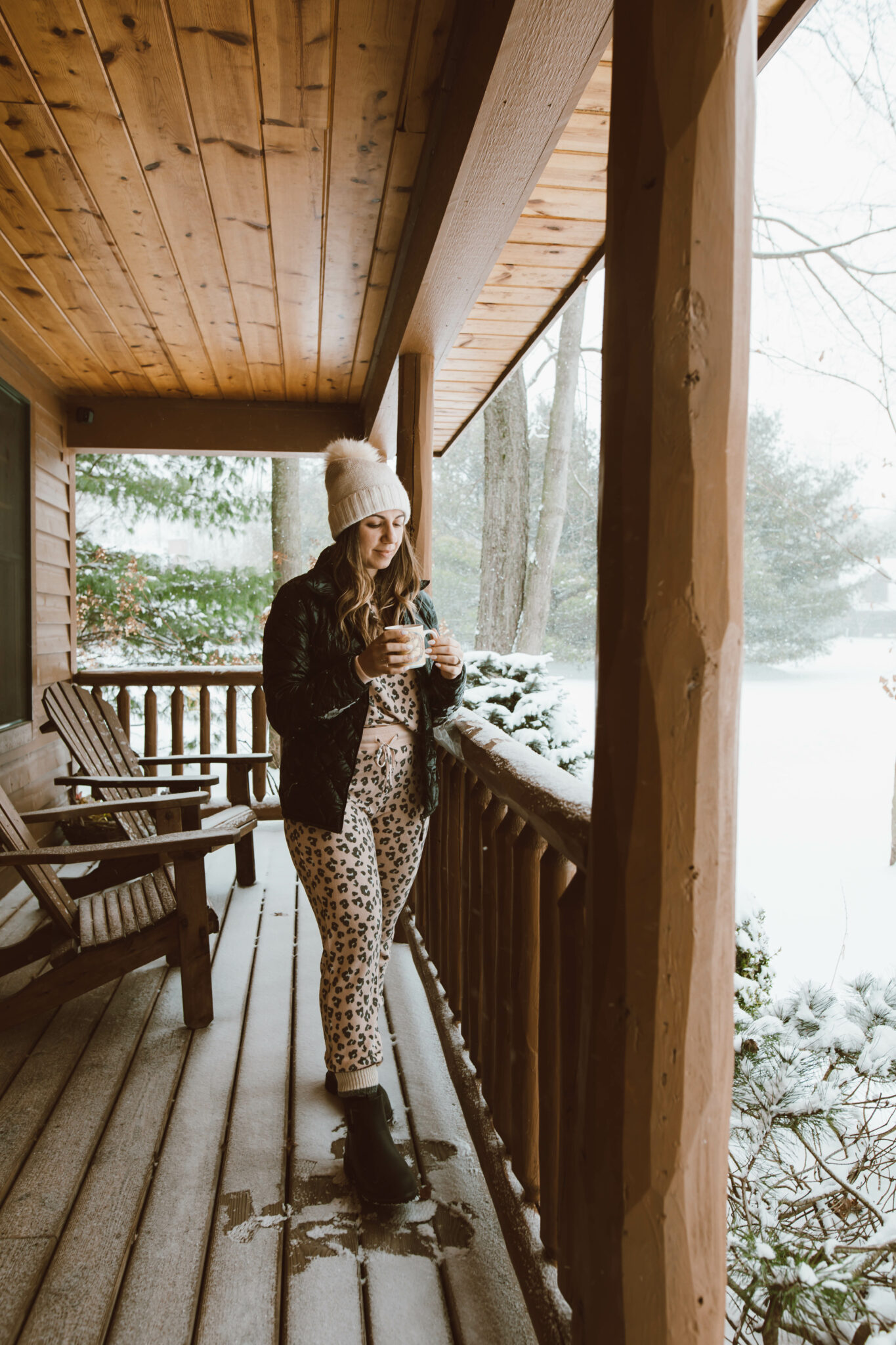 Loungewear Set by popular Chicago fashion blog, Glass of Glam: image of a woman standing on a cabin deck and wearing a leopard print loungewear set, quilted jacket and cream pom beanie. 