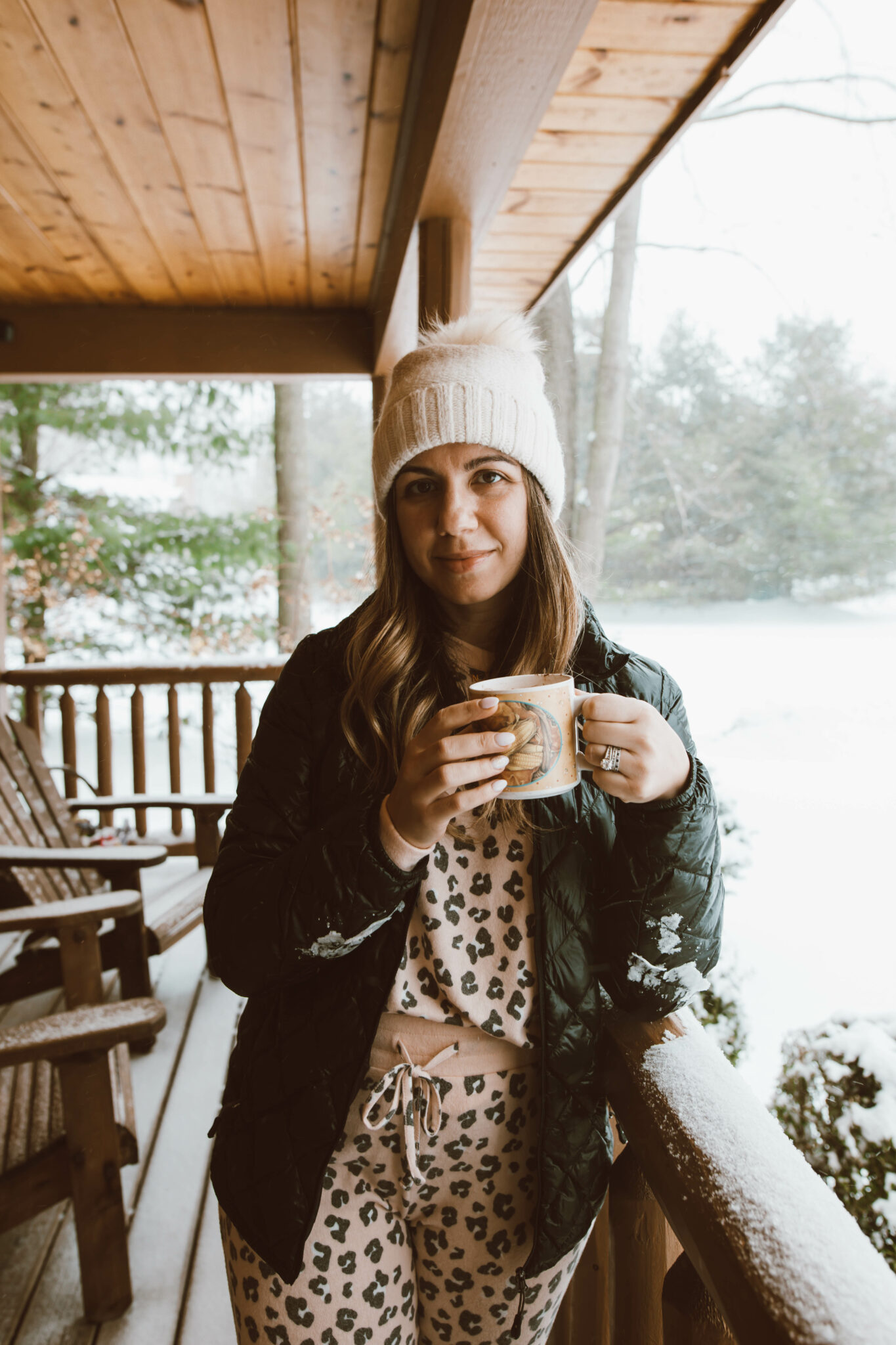 Loungewear Set by popular Chicago fashion blog, Glass of Glam: image of a woman standing on a cabin deck and wearing a leopard print loungewear set, quilted jacket and cream pom beanie.