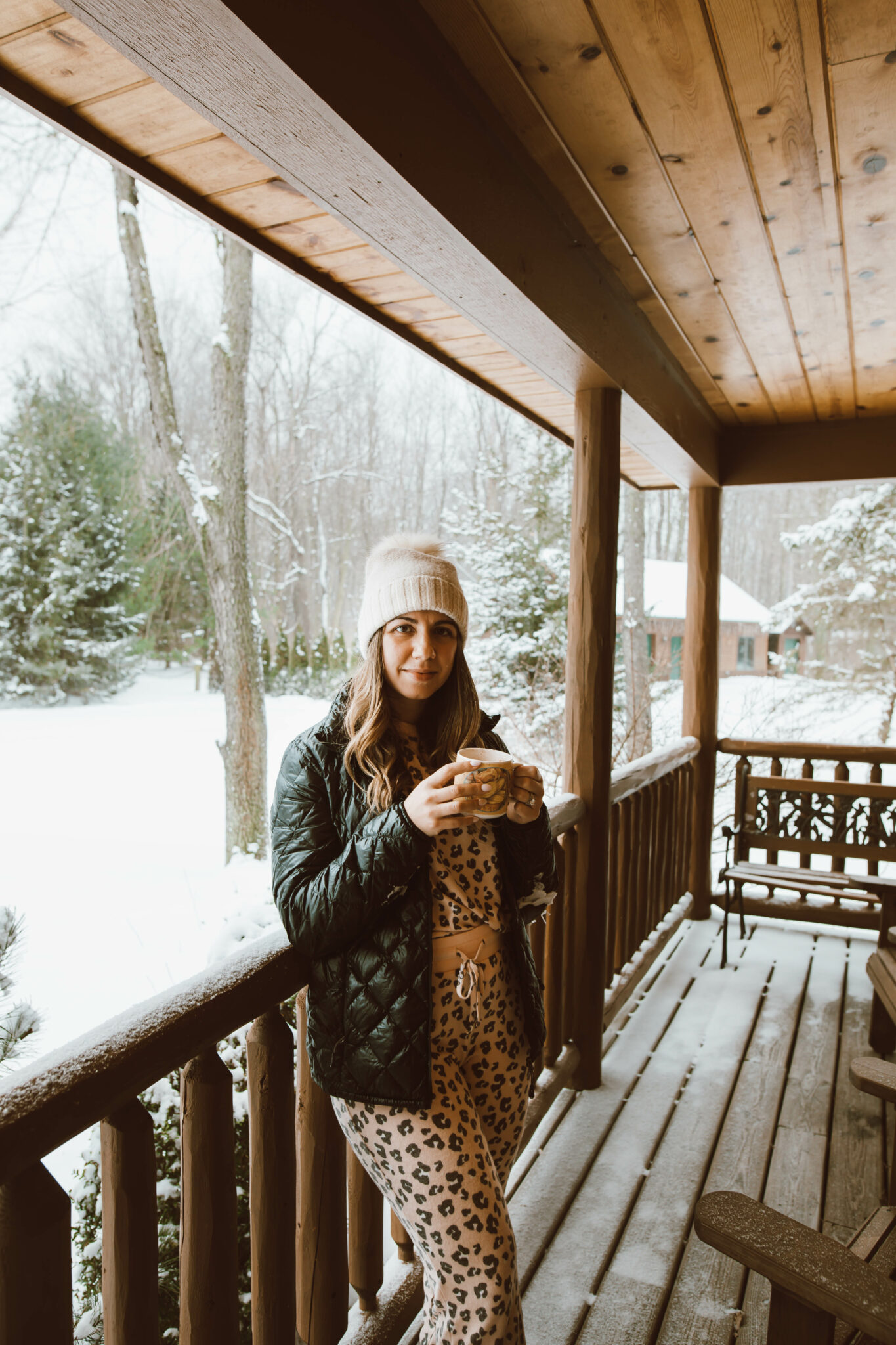 Loungewear Set by popular Chicago fashion blog, Glass of Glam: image of a woman standing on a cabin deck and wearing a leopard print loungewear set, quilted jacket and cream pom beanie. 