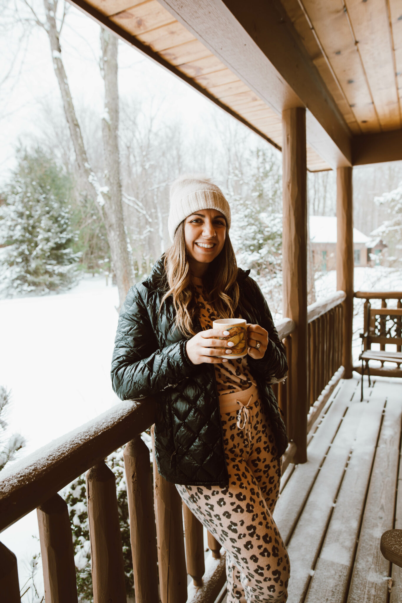 Loungewear Set by popular Chicago fashion blog, Glass of Glam: image of a woman standing on a cabin deck and wearing a leopard print loungewear set, quilted jacket and cream pom beanie.