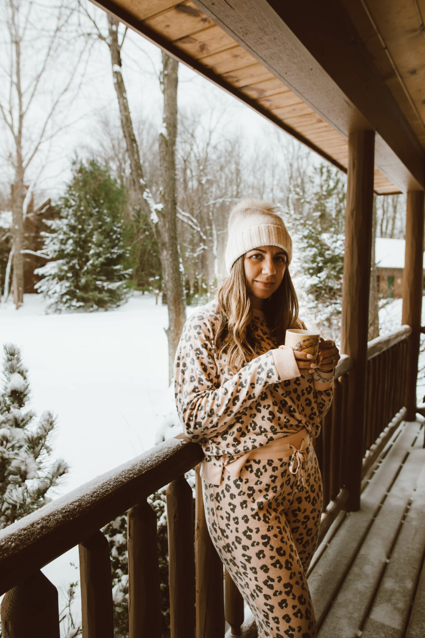 Loungewear Set by popular Chicago fashion blog, Glass of Glam: image of a woman standing on a cabin deck and wearing a leopard print loungewear set and cream pom beanie.