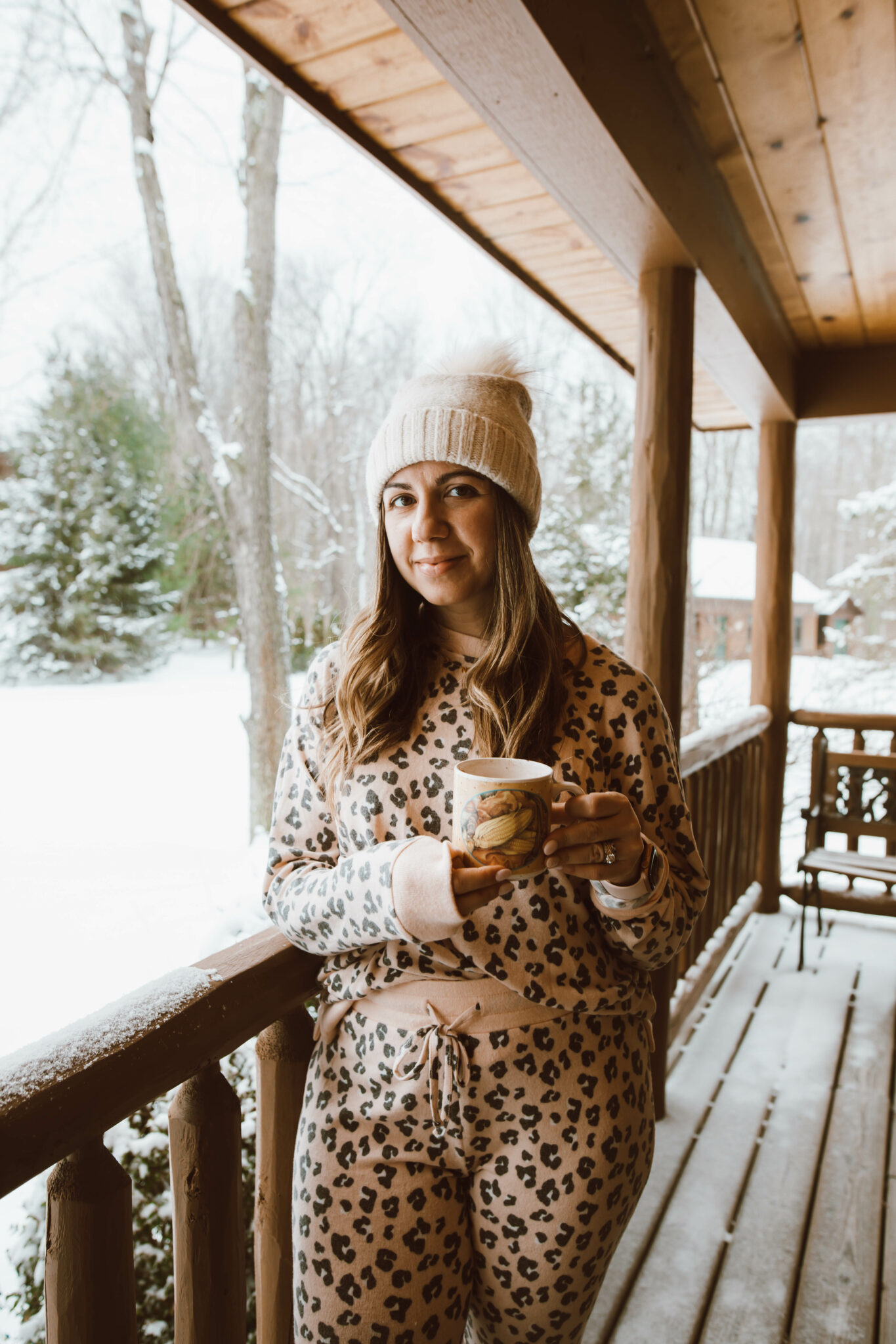 Loungewear Set by popular Chicago fashion blog, Glass of Glam: image of a woman standing on a cabin deck and wearing a leopard print loungewear set and cream pom beanie. 