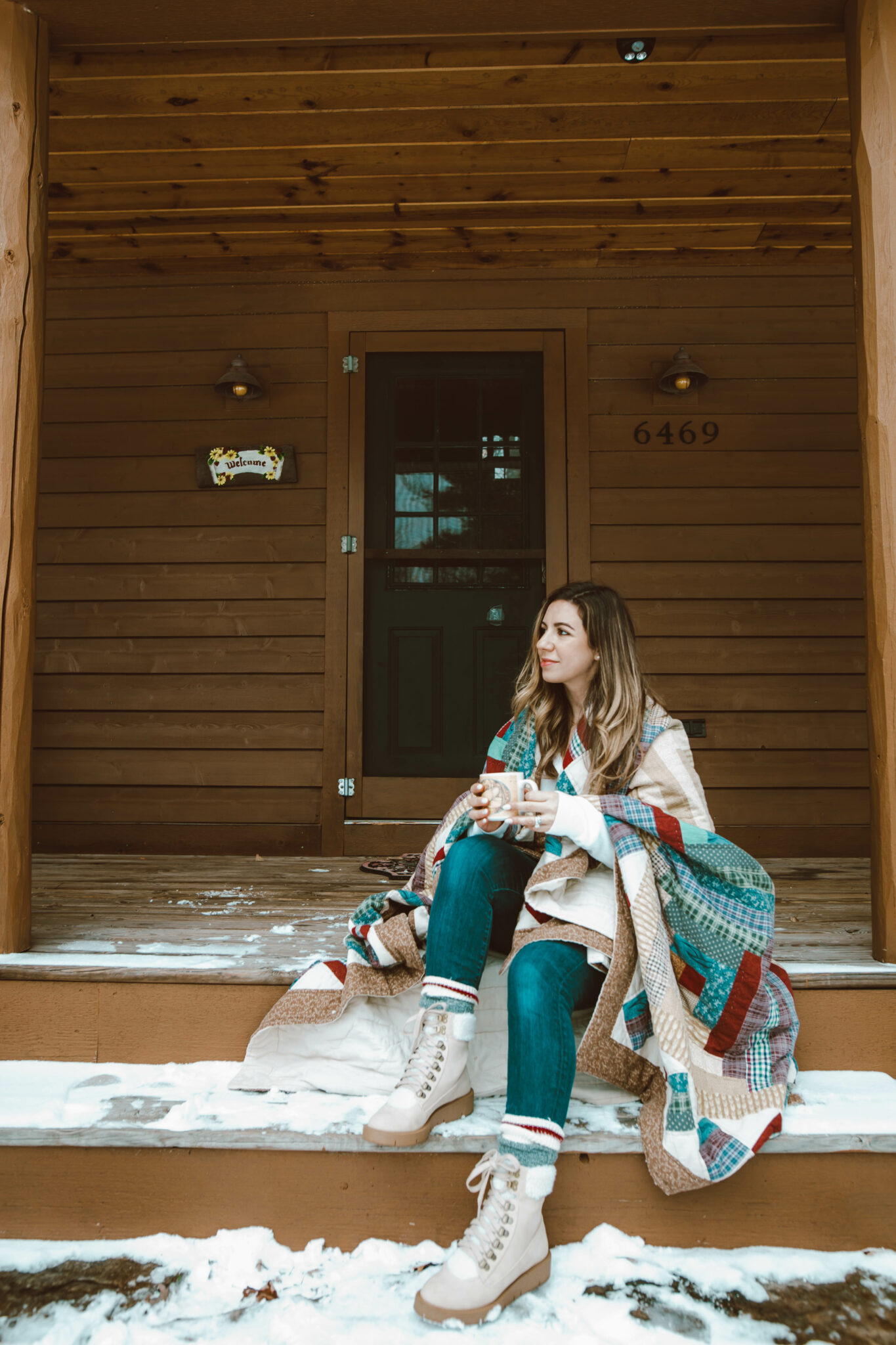 Fashion Basics by popular Chicago fashion blog, Glass of Glam: image of a woman sitting on outside of her cabin on the steps of her front porched wrapped up in a blanket and wearing a white henley t-shirt, jeans, JustFab hiking boots, and cabin socks.