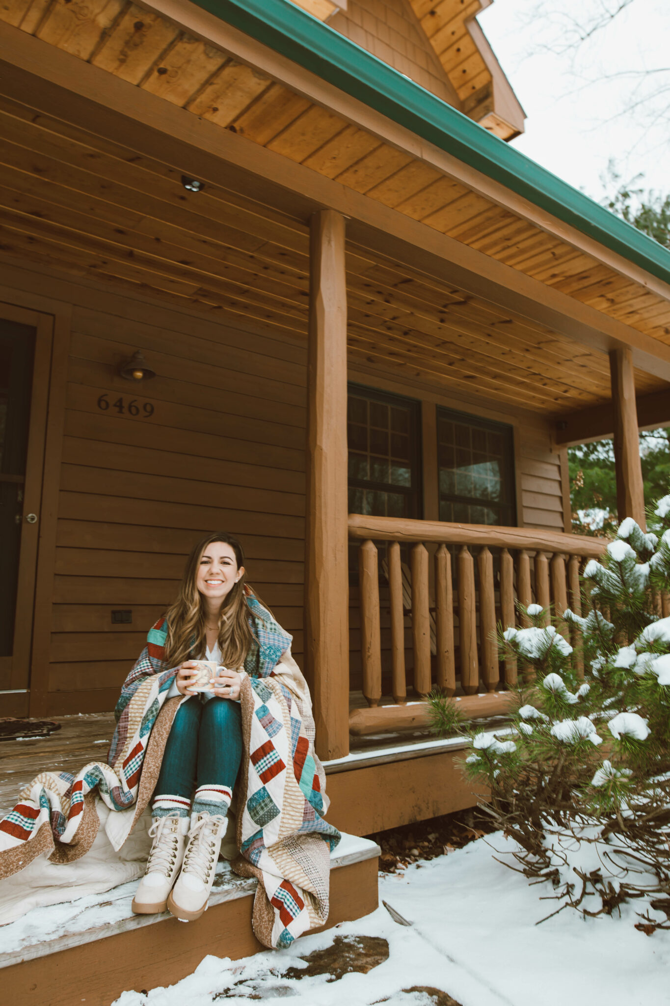 Fashion Basics by popular Chicago fashion blog, Glass of Glam: image of a woman sitting on outside of her cabin on the steps of her front porched wrapped up in a blanket and wearing a white henley t-shirt, jeans, JustFab hiking boots, and cabin socks.