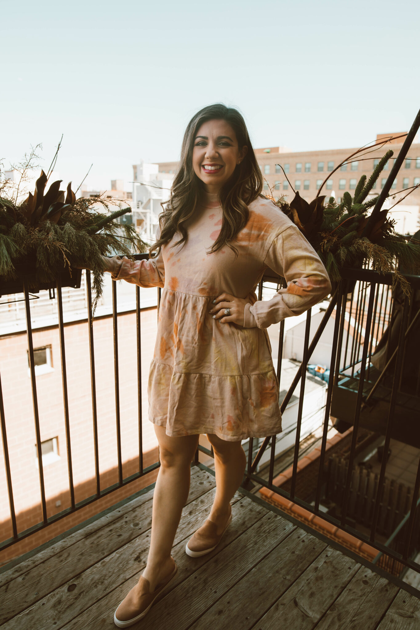 Tie Dye Dresses by popular Chicago fashion blog, Glass of Glam: image of a woman standing on her balcony and wearing a orange tie dye dress and brown slip on sneakers. 