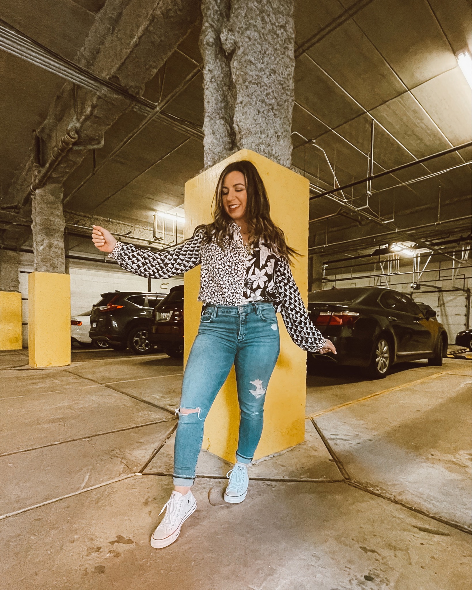 Tucked Shirt by popular Chicago fashion blog, Glass of Glam: image of a woman standing in a parking garage and wearing a black and white mixed print button up shirt, distressed denim, and white Converse sneakers. 