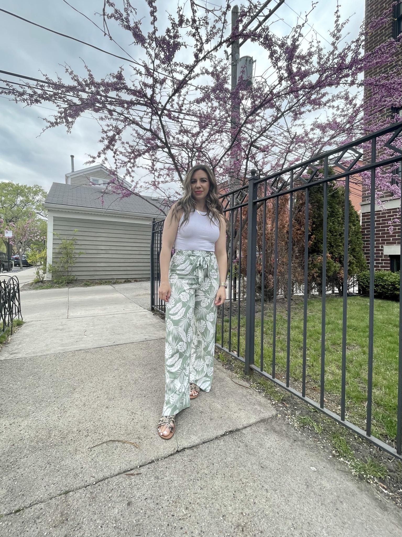 Statement Pants by popular Chicago fashion blog, Glass of Glam: image of a woman standing outside and wearing a pair of green tie waist leaf print pants, slide sandals, and a white tank top.