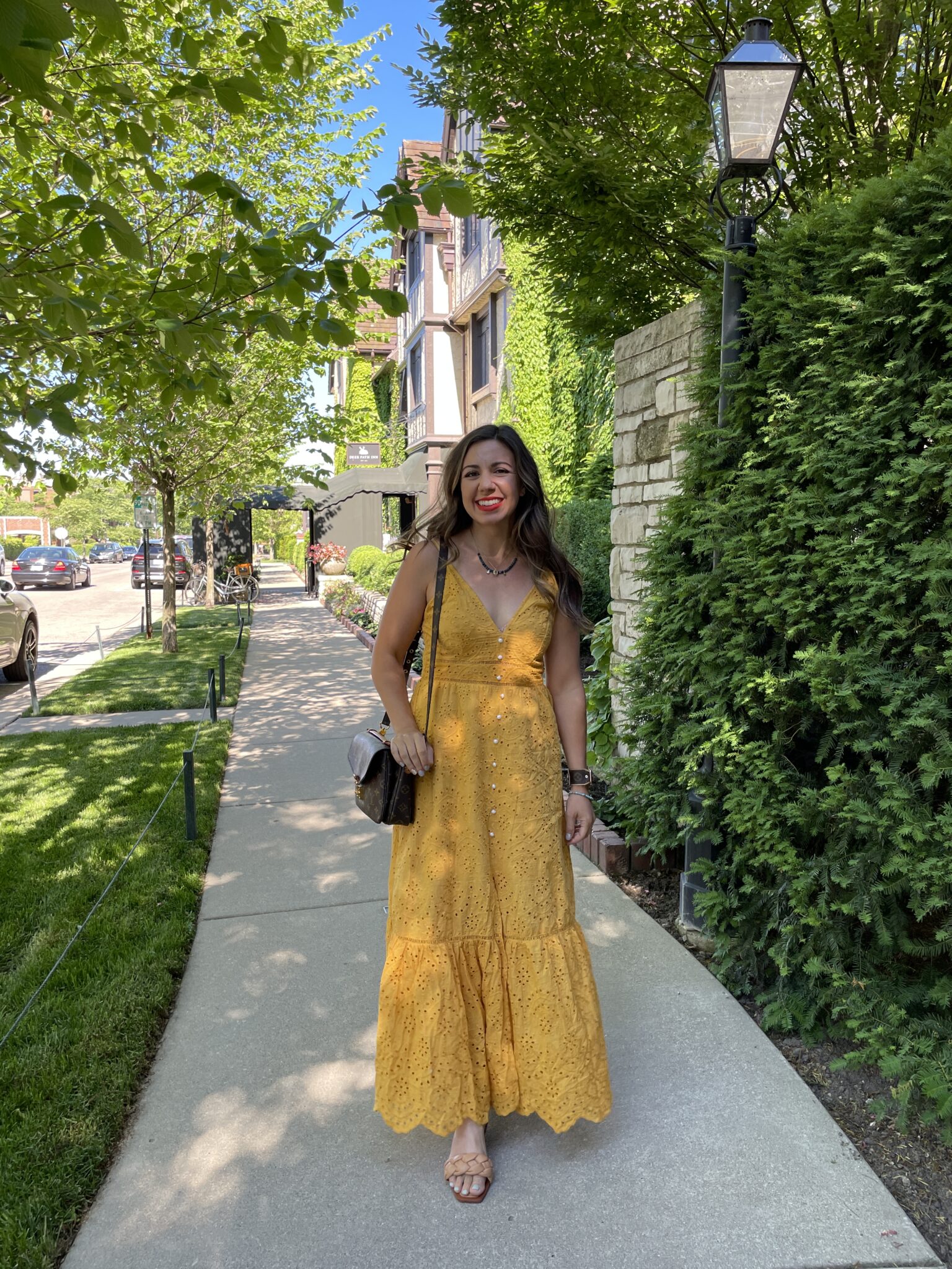 Eyelet Clothing by popular Chicago fashion blog, Glass of Glam: image of a woman walking outside next to a fence covered in ivy and wearing a yellow eyelet maxi dress with tan braided sandals and a silpada necklace. 