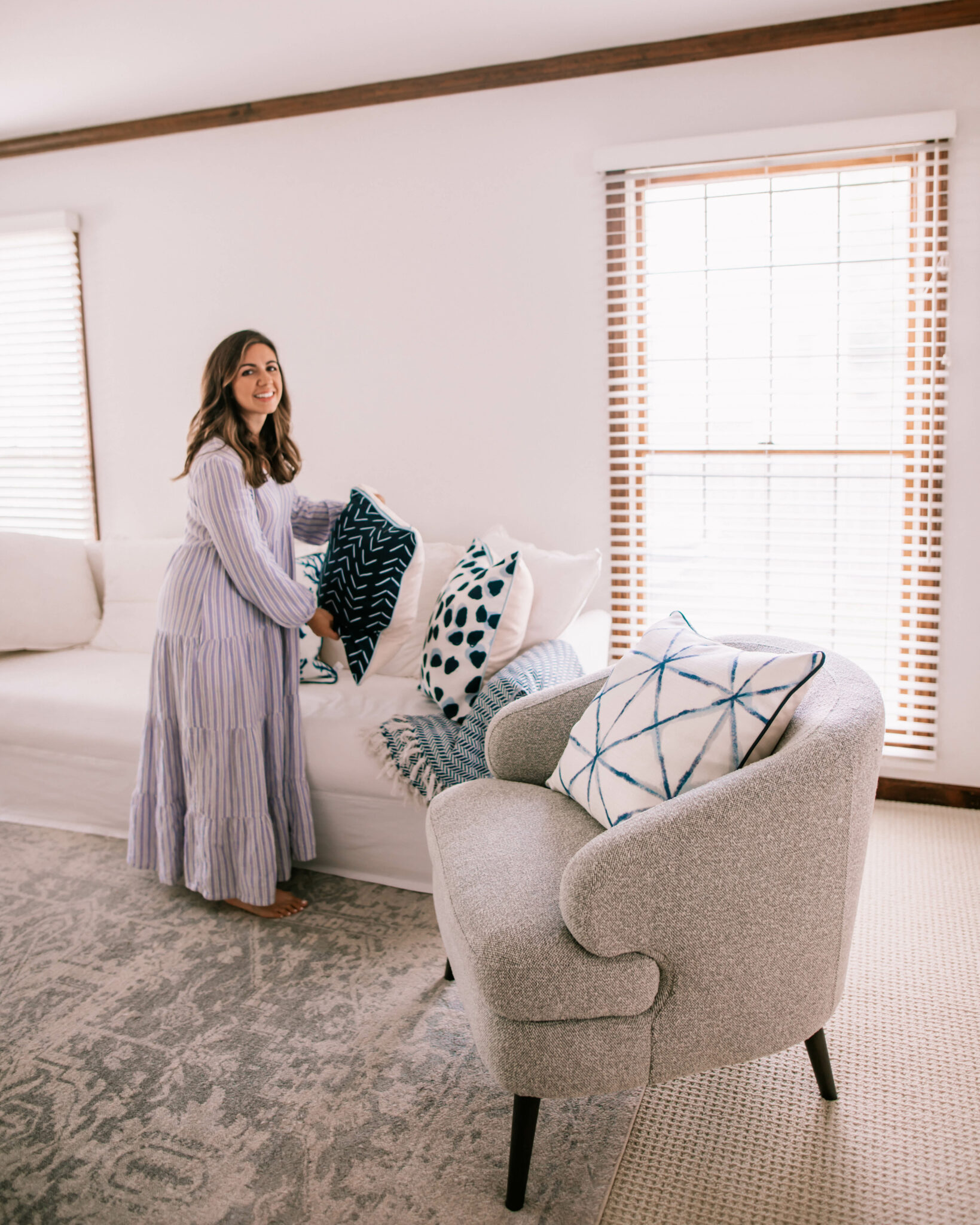 Thomasville Furniture by popular Chicago life and style blog, Glass of Glam: image of a woman wearing a purple stripe maxi dress and standing in a living room decorated with a white couch, blue, grey and white accent rug, grey armchair, and blue and white throw pillows. 